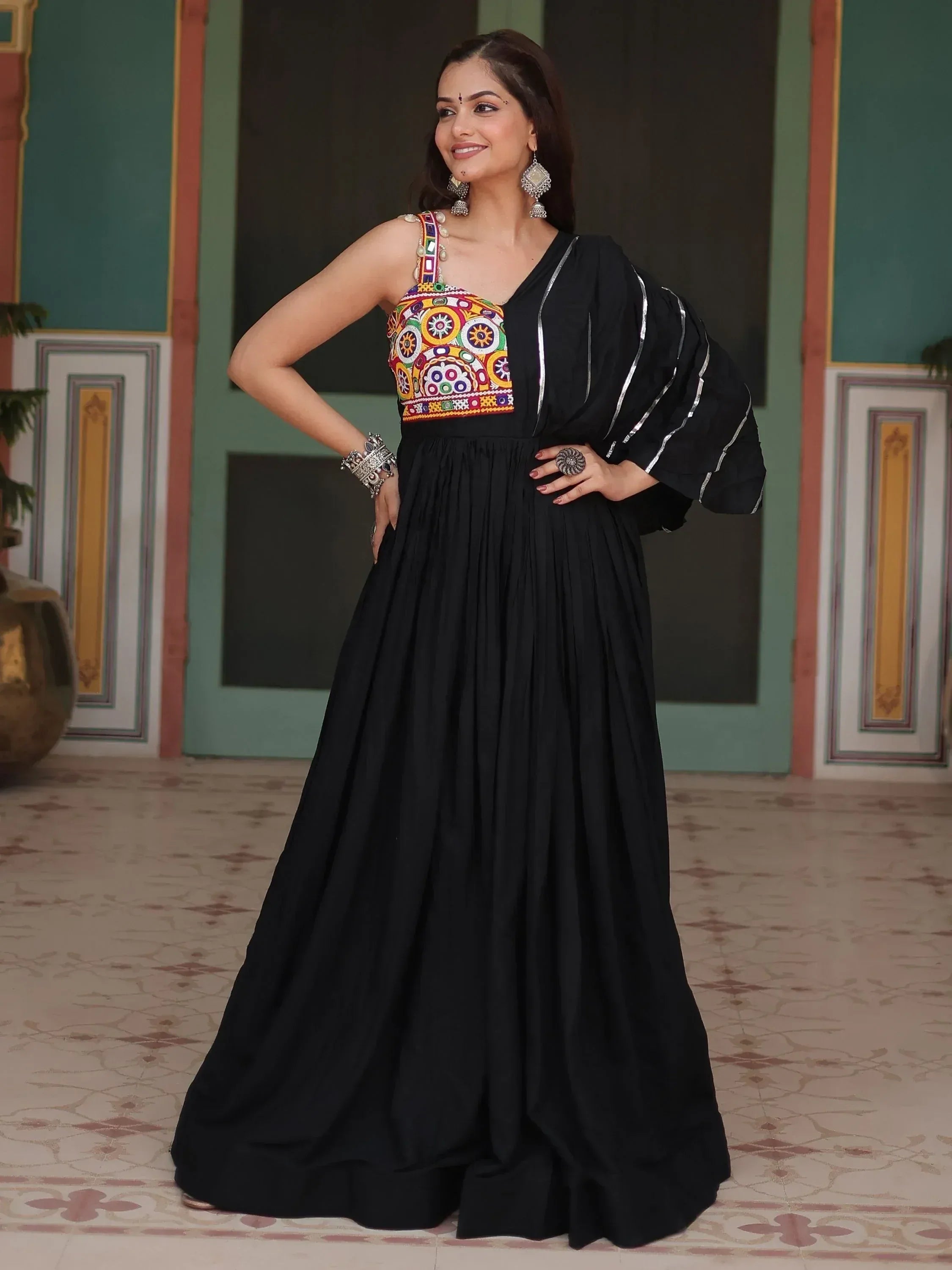 Woman in black ethnic gown with colorful embroidered bodice, traditional jewelry, indoor setting