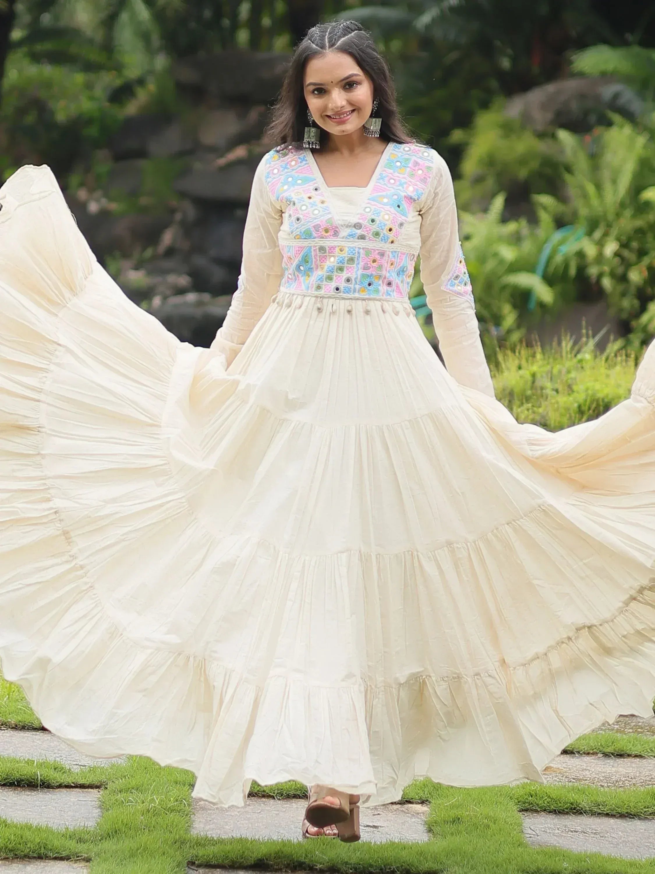 Woman wearing cream ethnic gown with colorful mirror work, flared skirt, outdoor garden background