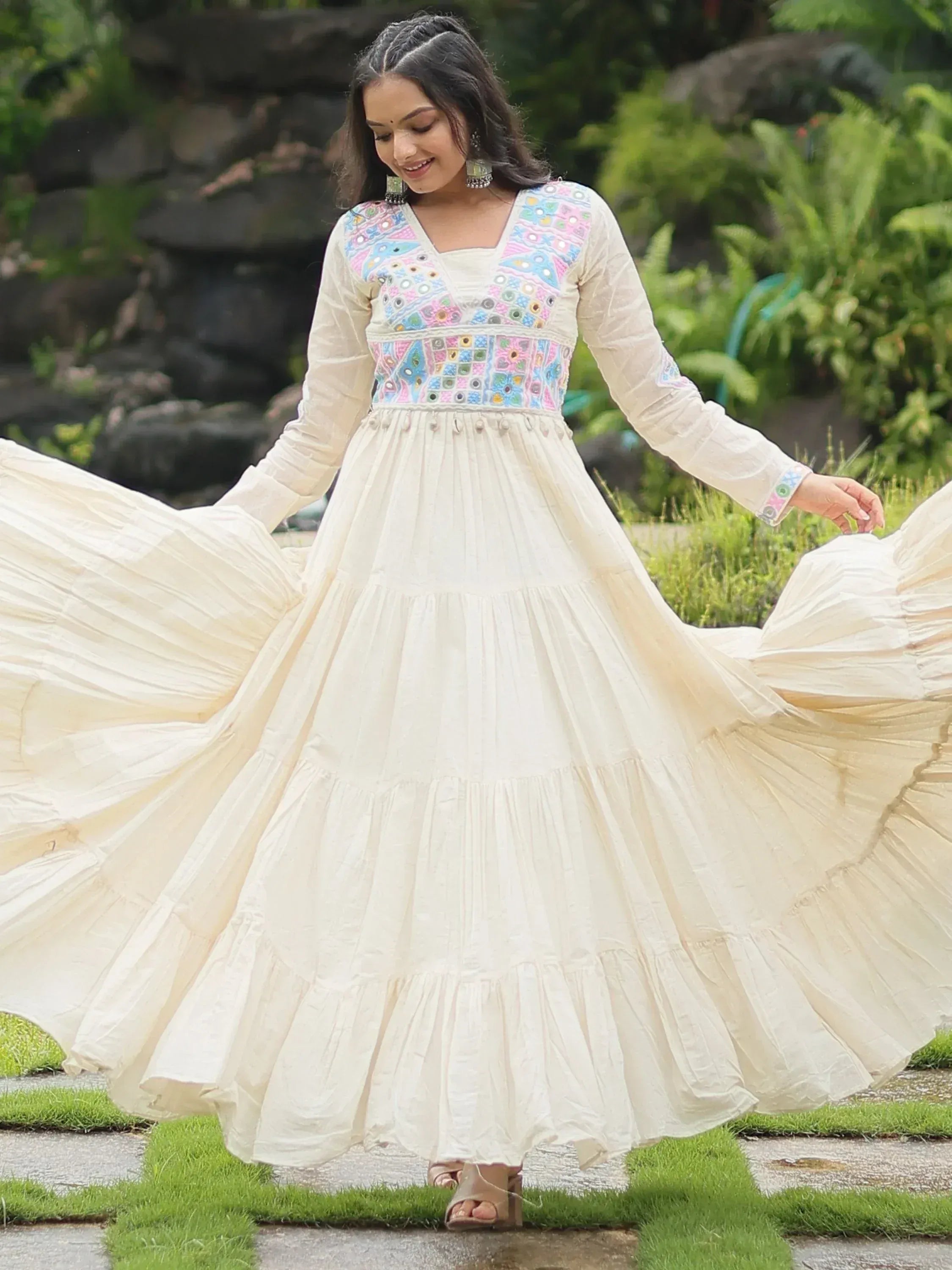 Woman in cream Anarkali gown with colorful embroidered yoke, posing outdoors