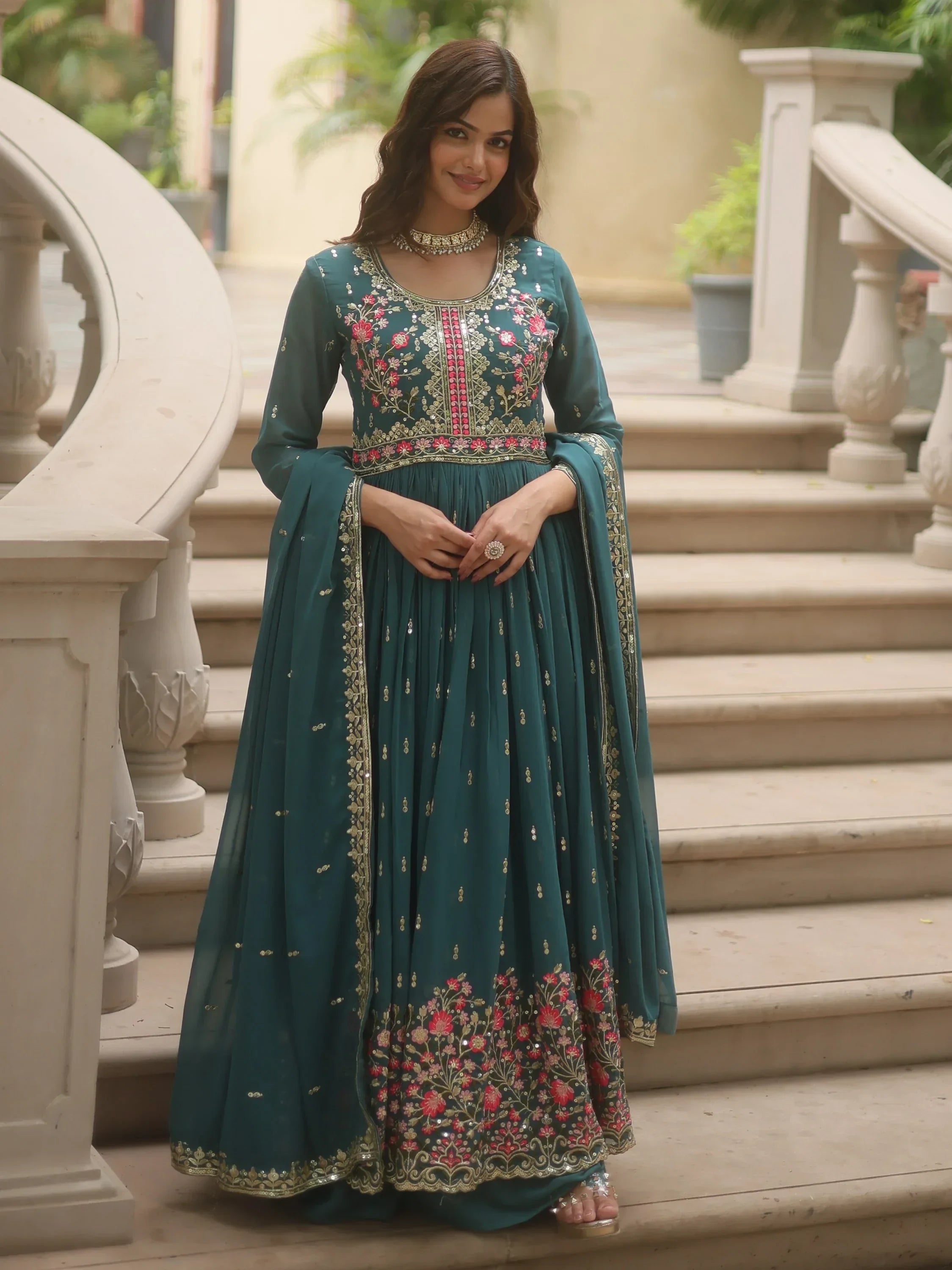 Woman in teal embroidered ethnic gown with floral designs standing on staircase