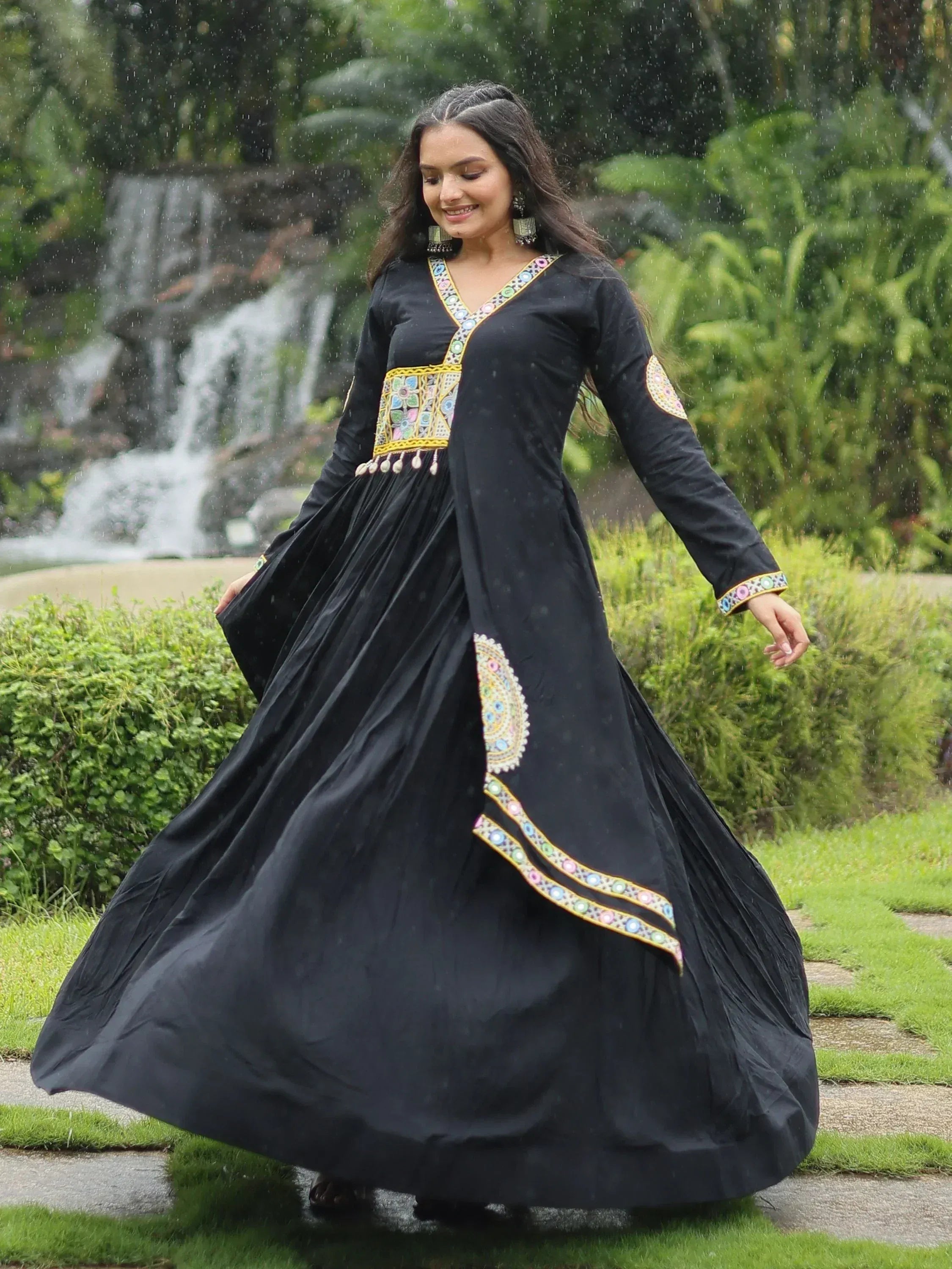 Black ethnic gown with colorful mirror work, worn in rain near waterfall, perfect for festive occasions.
