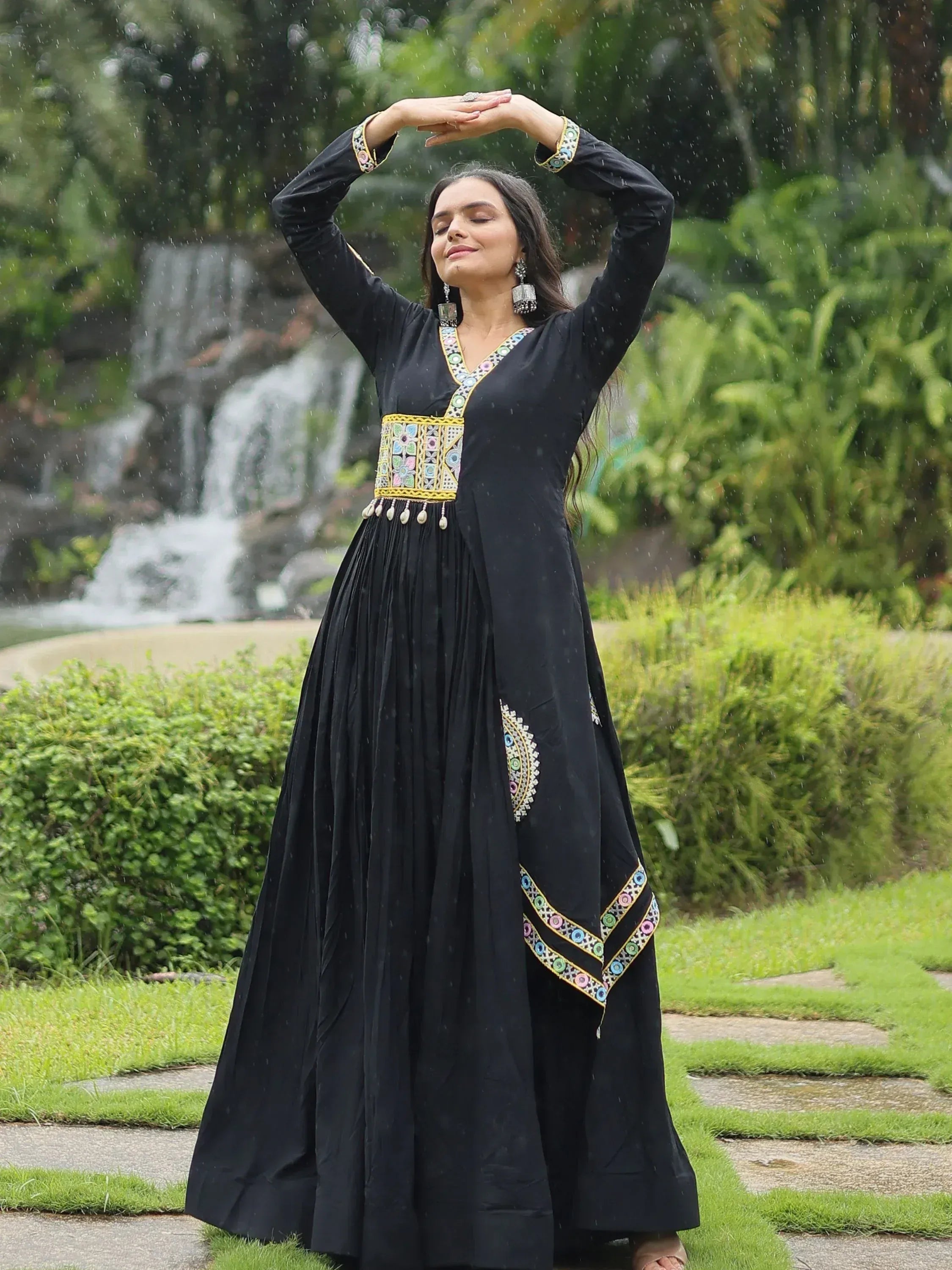 Black embroidered ethnic gown with colorful mirror work, worn in rain near waterfall