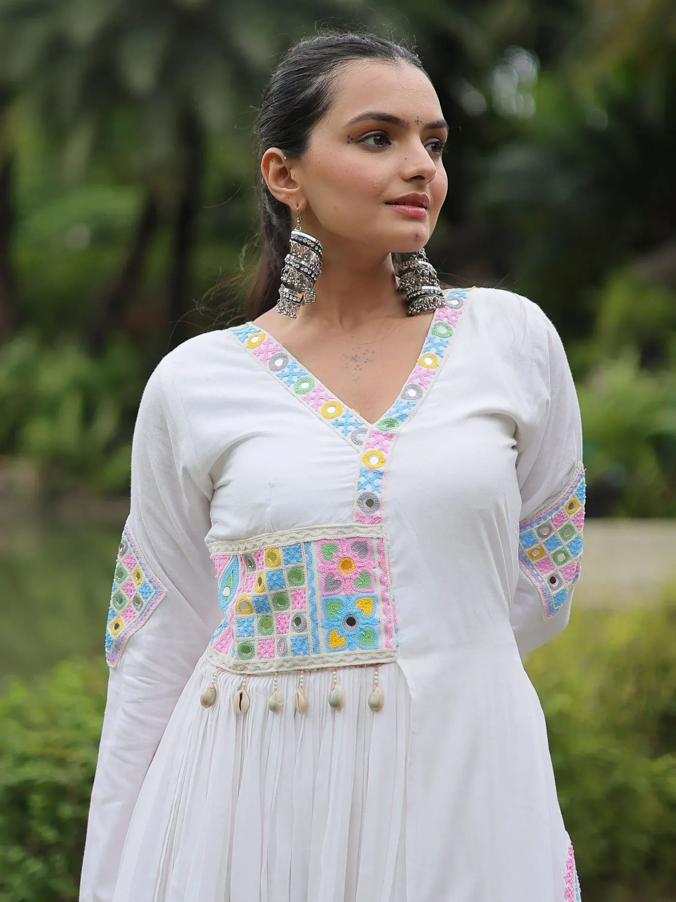 White ethnic kurta with colorful mirror embroidery and shell tassels, paired with statement earrings