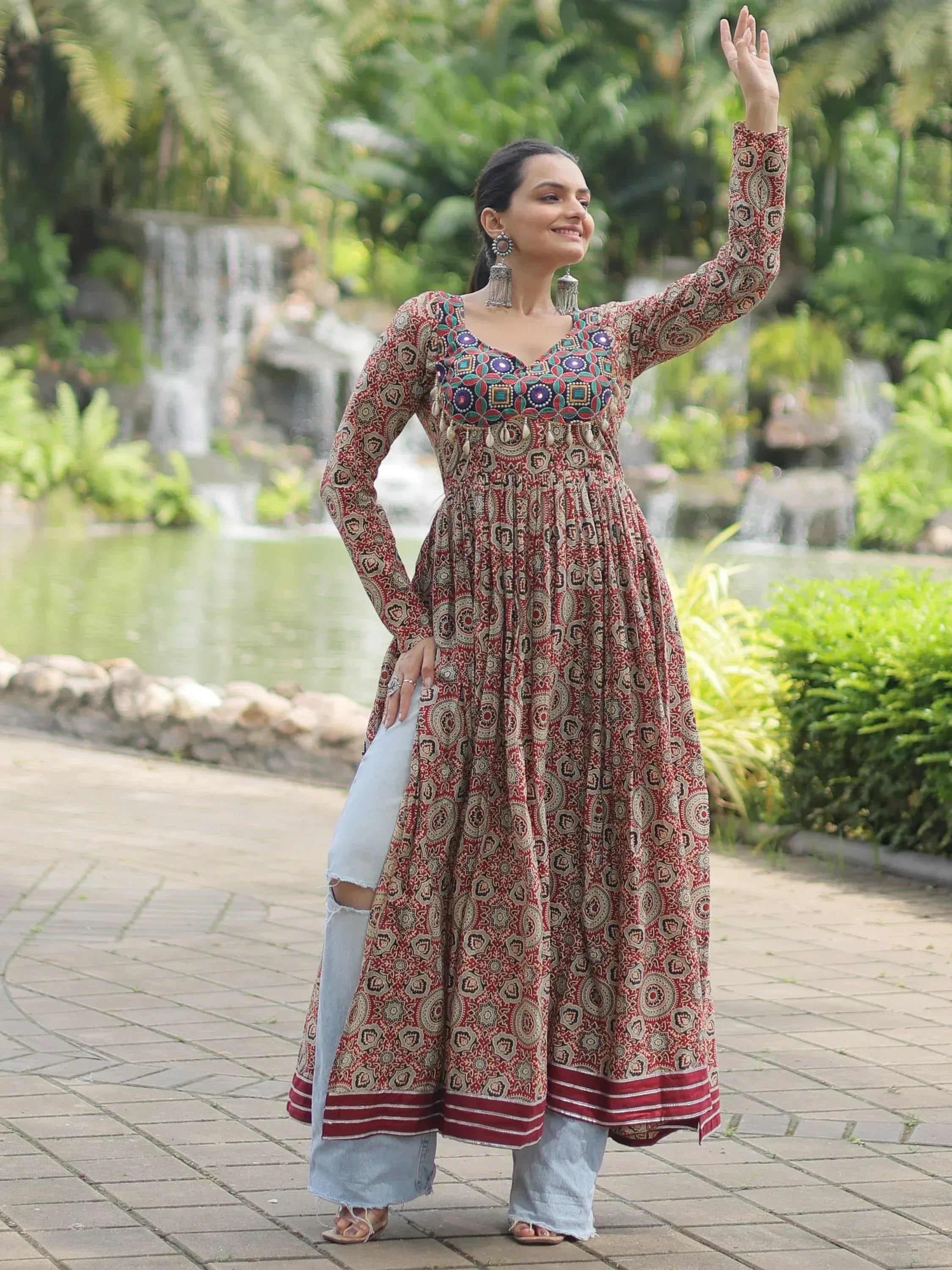 Woman in red printed ethnic kurta with mirror work, paired with ripped jeans, standing in garden