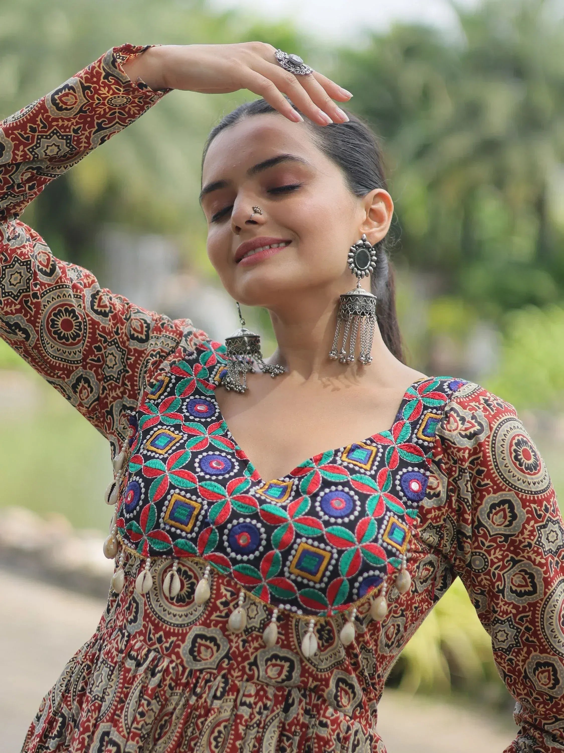 Woman in colorful embroidered ethnic gown with mirror work, jhumka earrings, and nose ring, outdoors