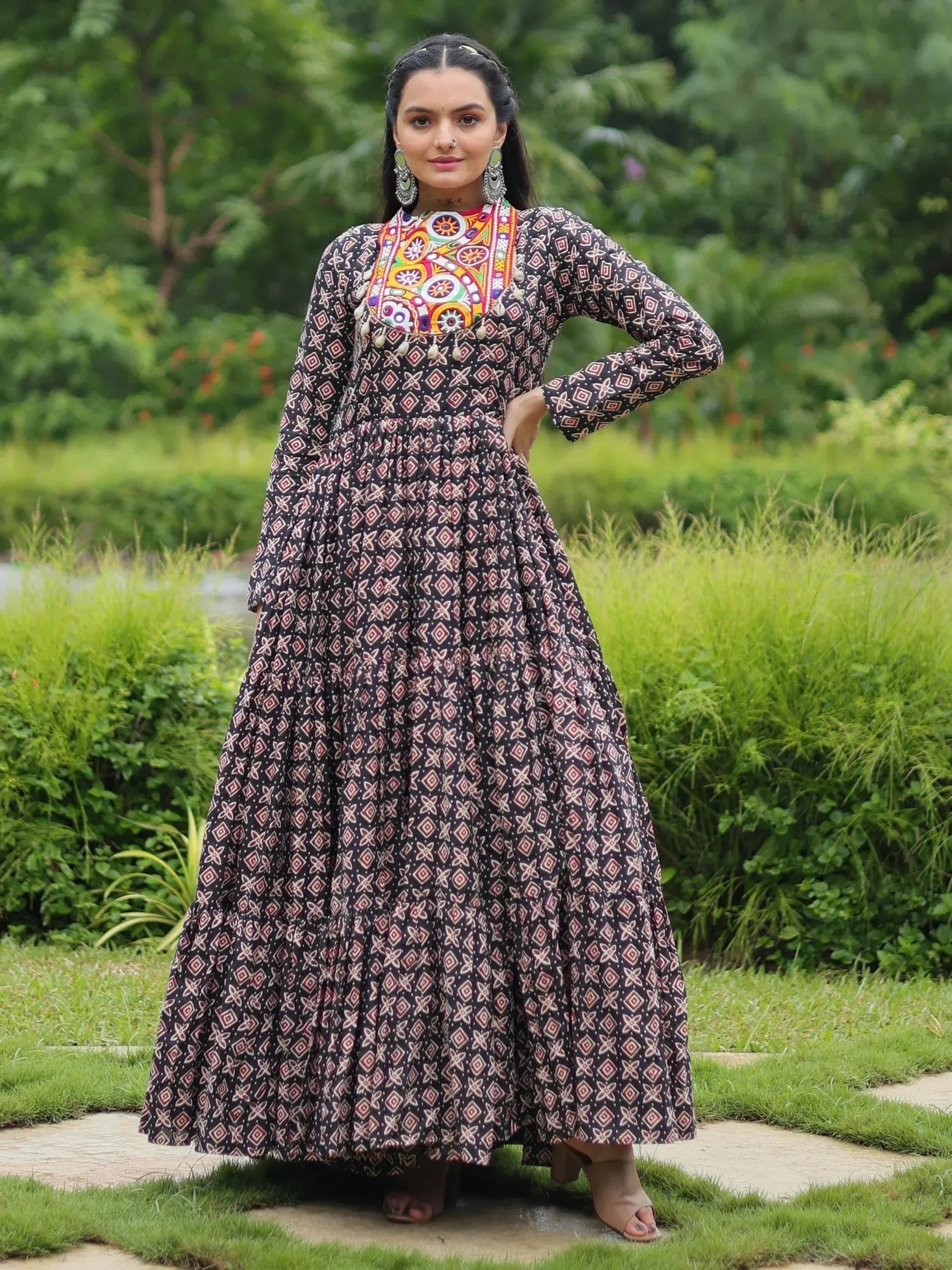 Woman in black printed ethnic gown with colorful embroidered neckline, standing outdoors