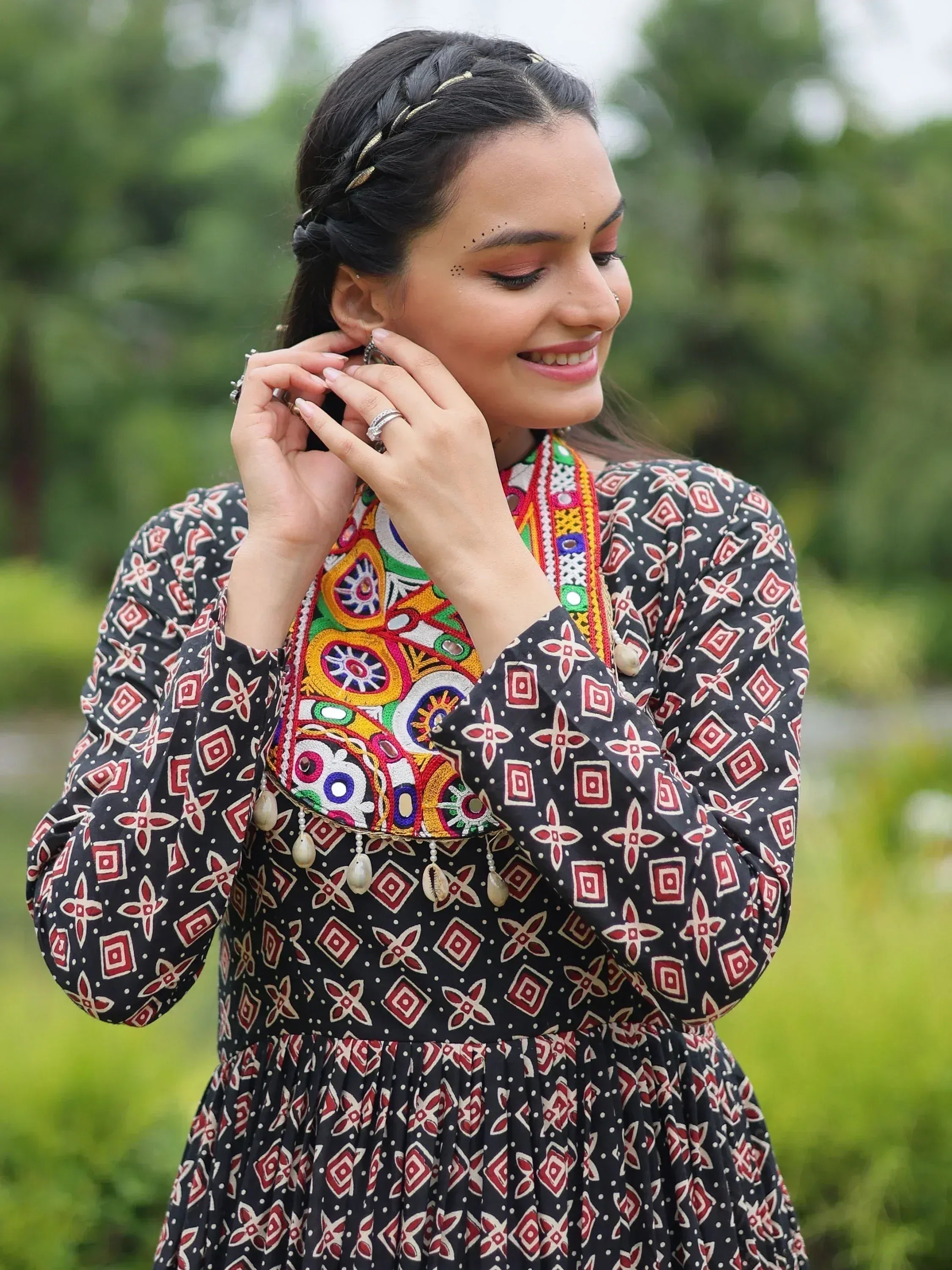 Woman in black ethnic dress with colorful mirror work and geometric print, adjusting earrings outdoors