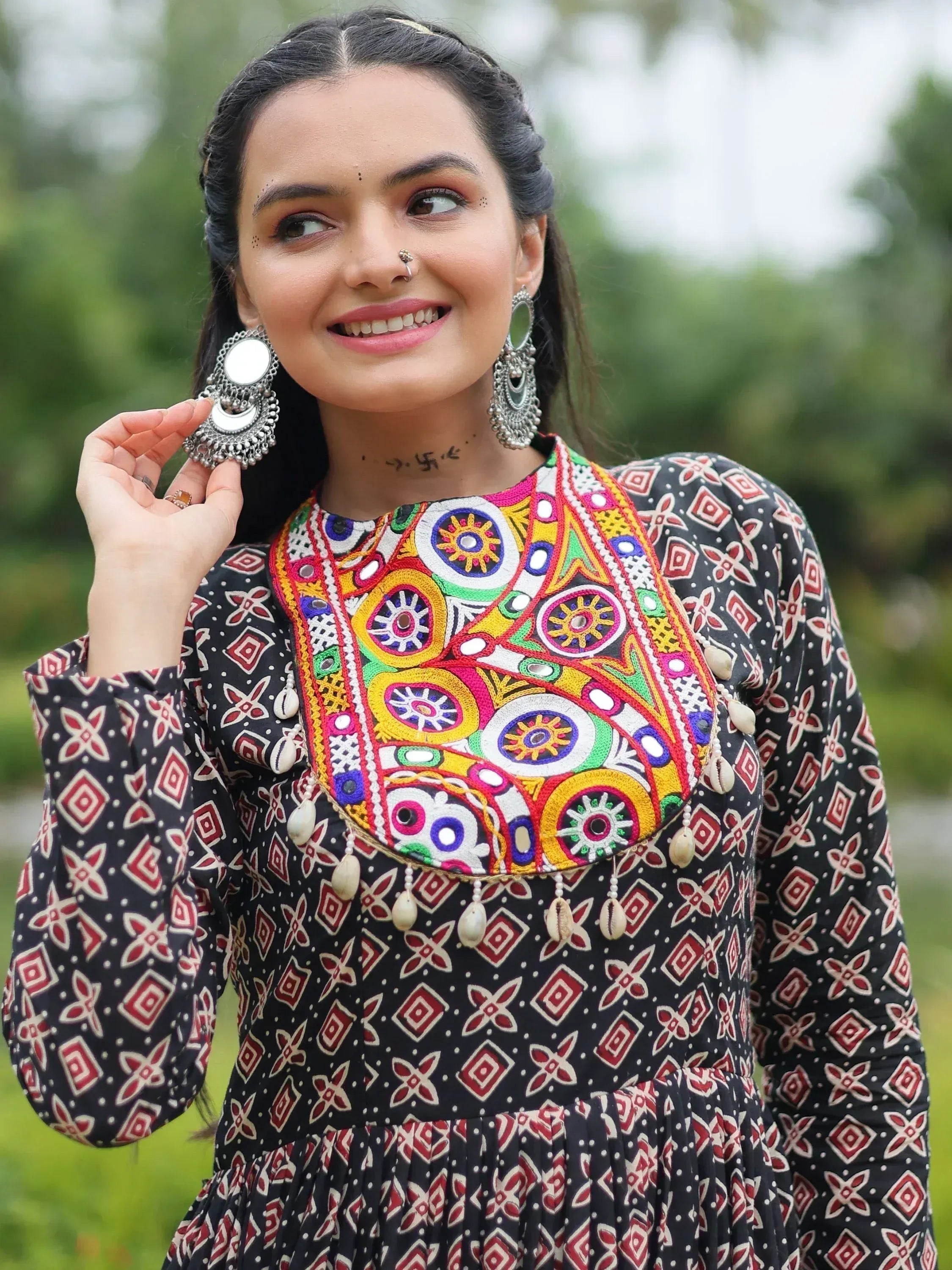 Woman in colorful embroidered ethnic dress with mirror work and statement earrings, perfect for Indian festivals or weddings.