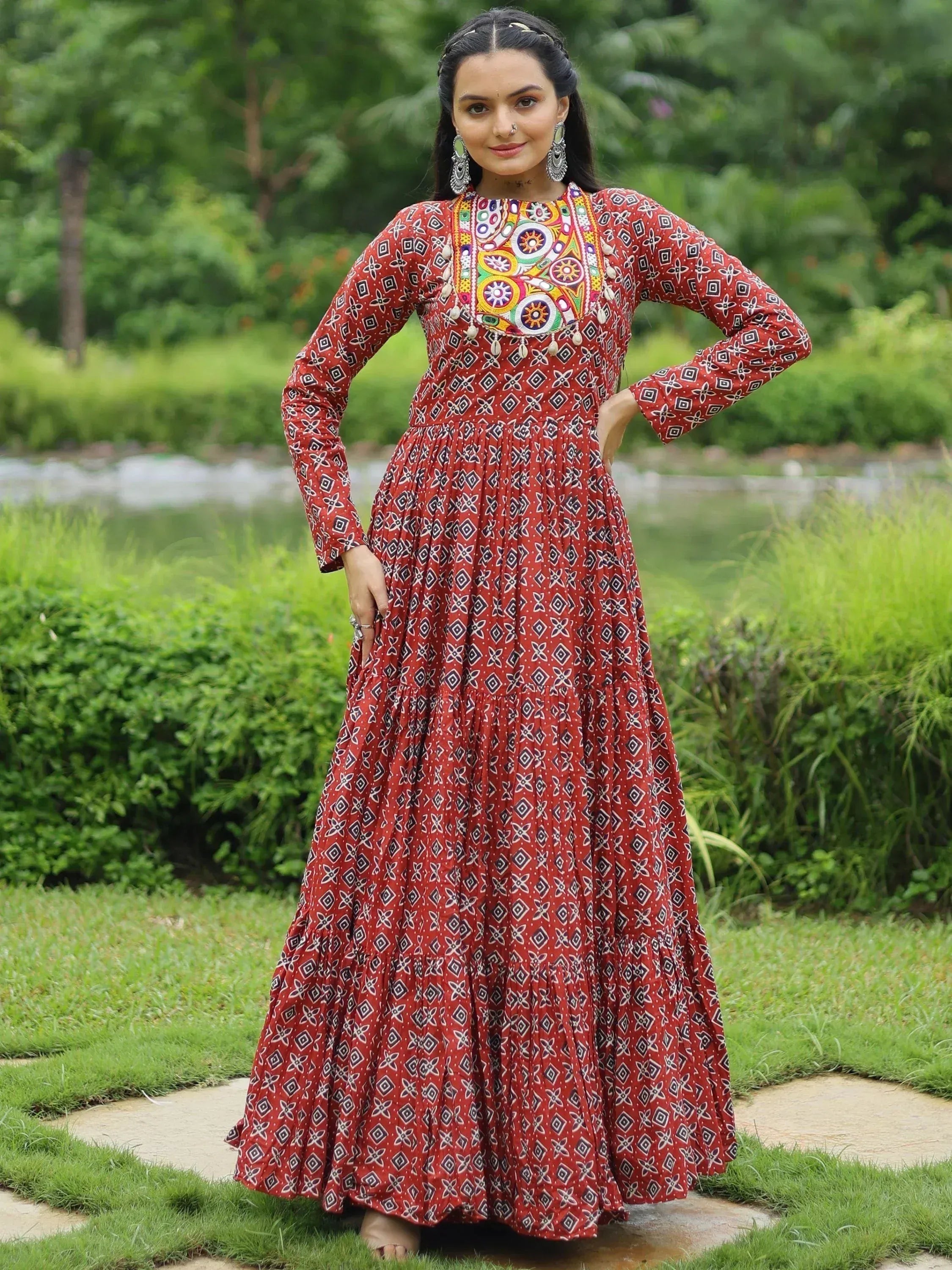 Woman in red printed ethnic gown with colorful embroidery, standing in garden