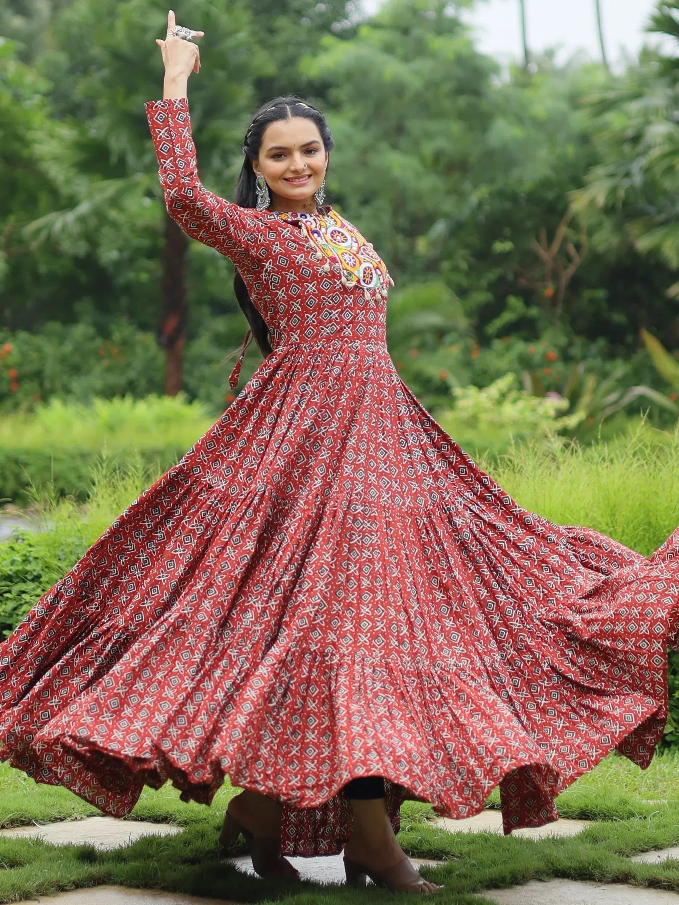 Woman in red printed ethnic gown with flared skirt, dancing outdoors in garden