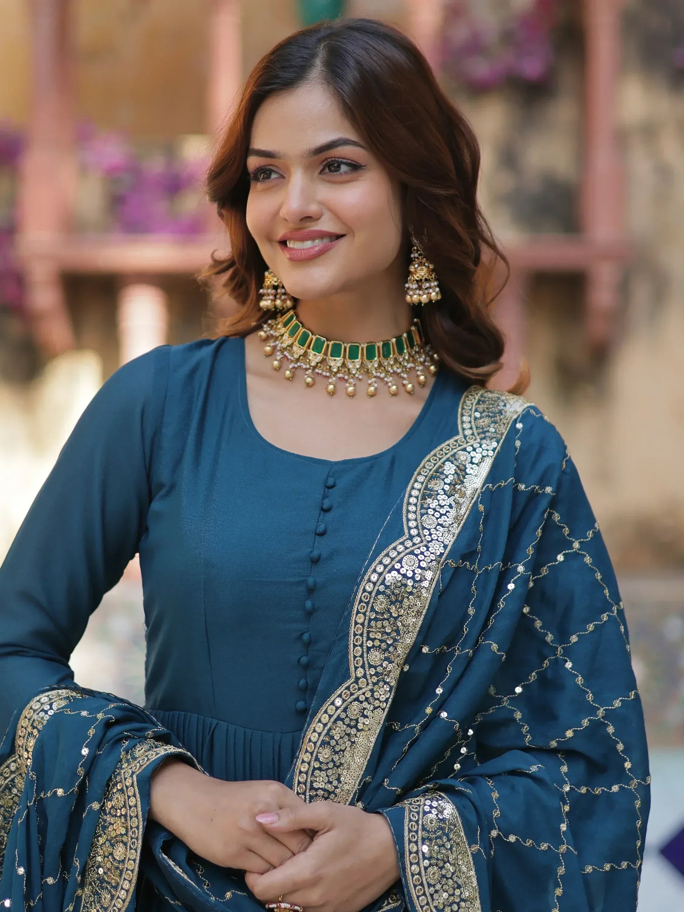 Woman in teal ethnic salwar kameez with gold embroidery and green jewelry