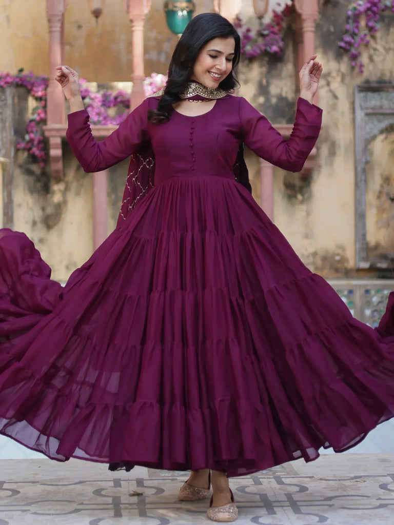 Woman twirling in a maroon ethnic gown with layered skirt and gold embroidery, perfect for festive occasions.
