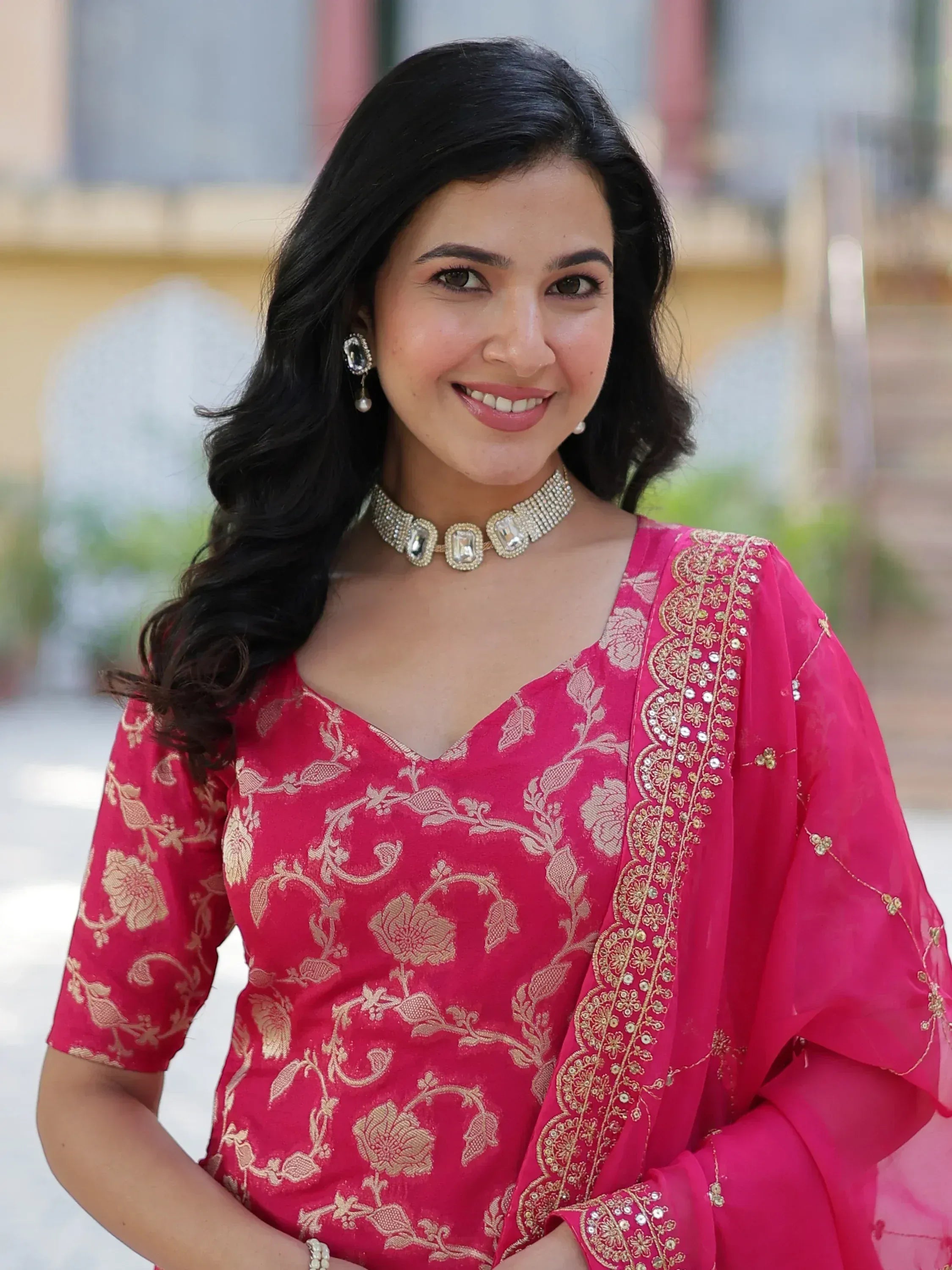 Woman in pink floral embroidered Indian ethnic wear with gold detailing and statement jewelry