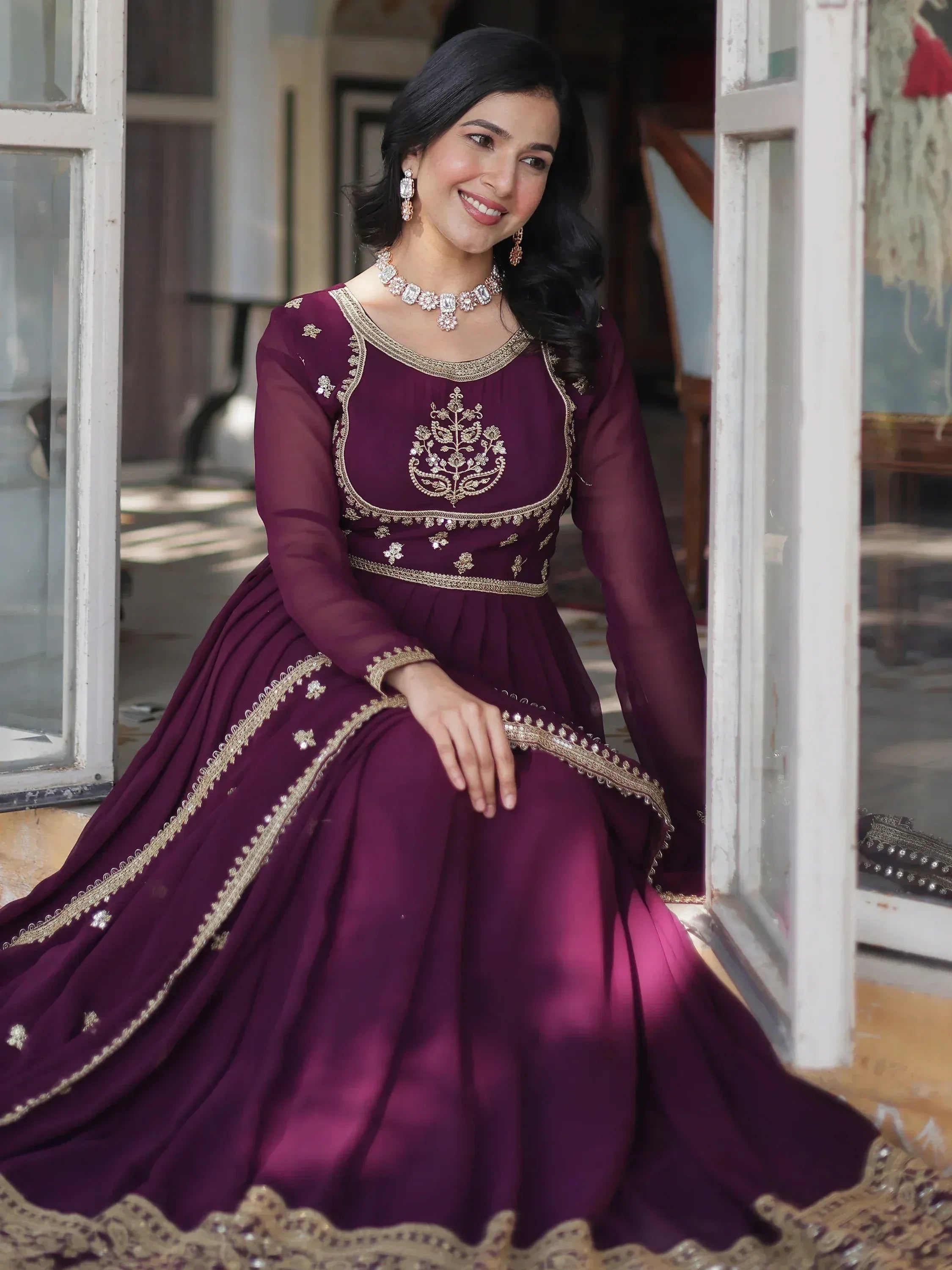 Woman in maroon embroidered ethnic gown with gold detailing, perfect for Indian weddings or festive occasions.
