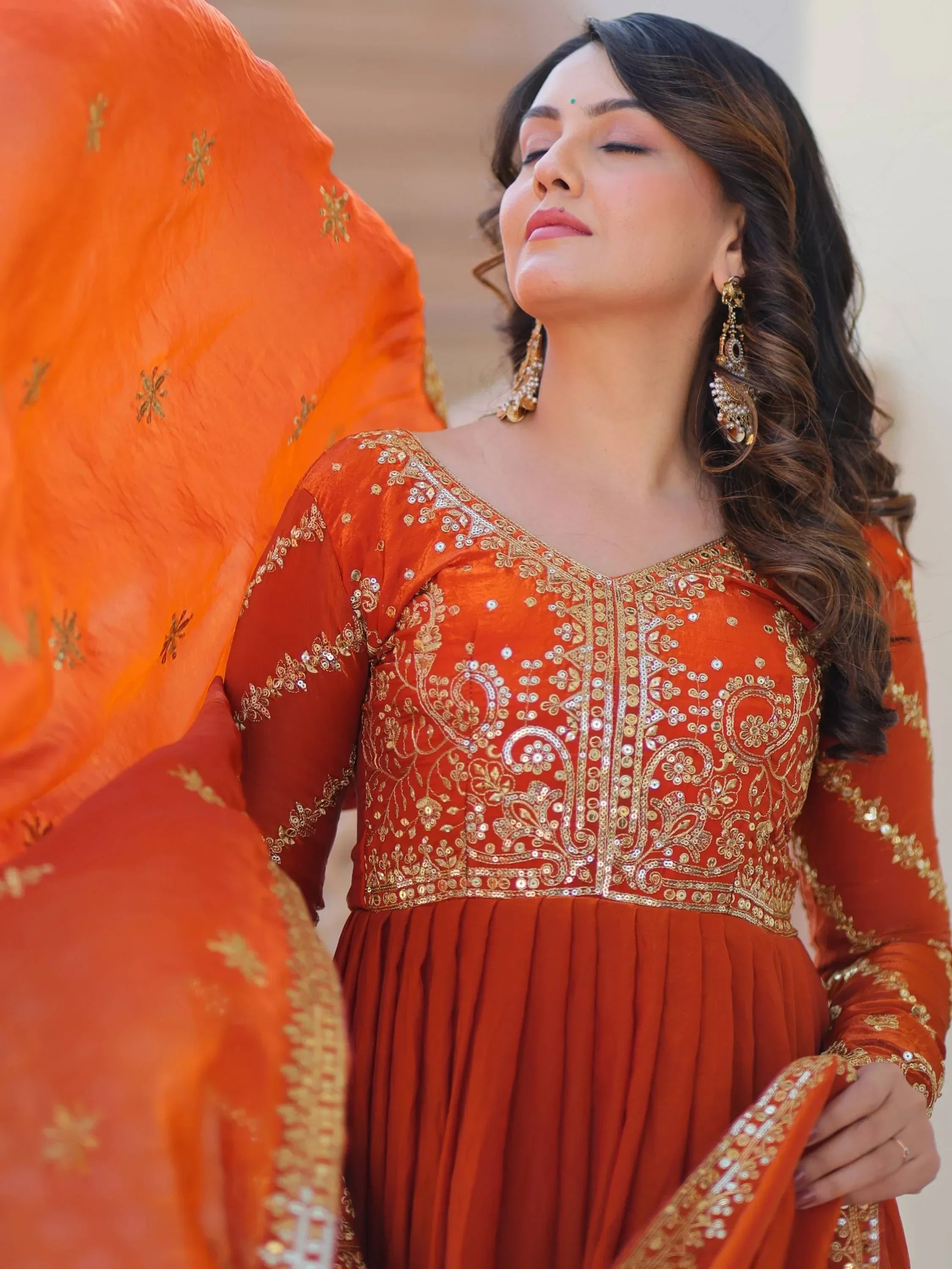 Woman in orange embroidered ethnic gown with gold detailing and statement earrings