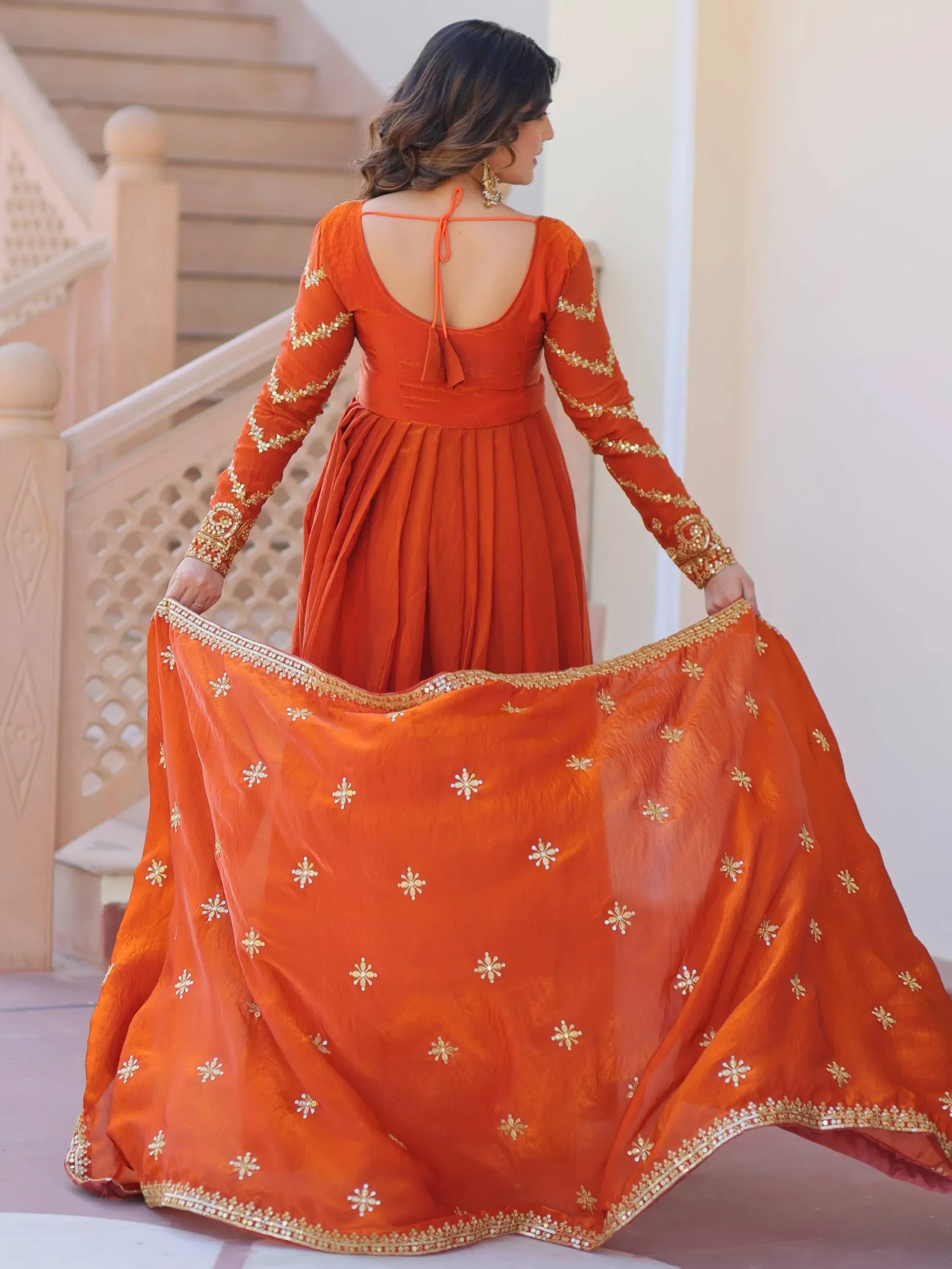 Woman in orange embroidered ethnic gown with gold detailing, holding matching dupatta