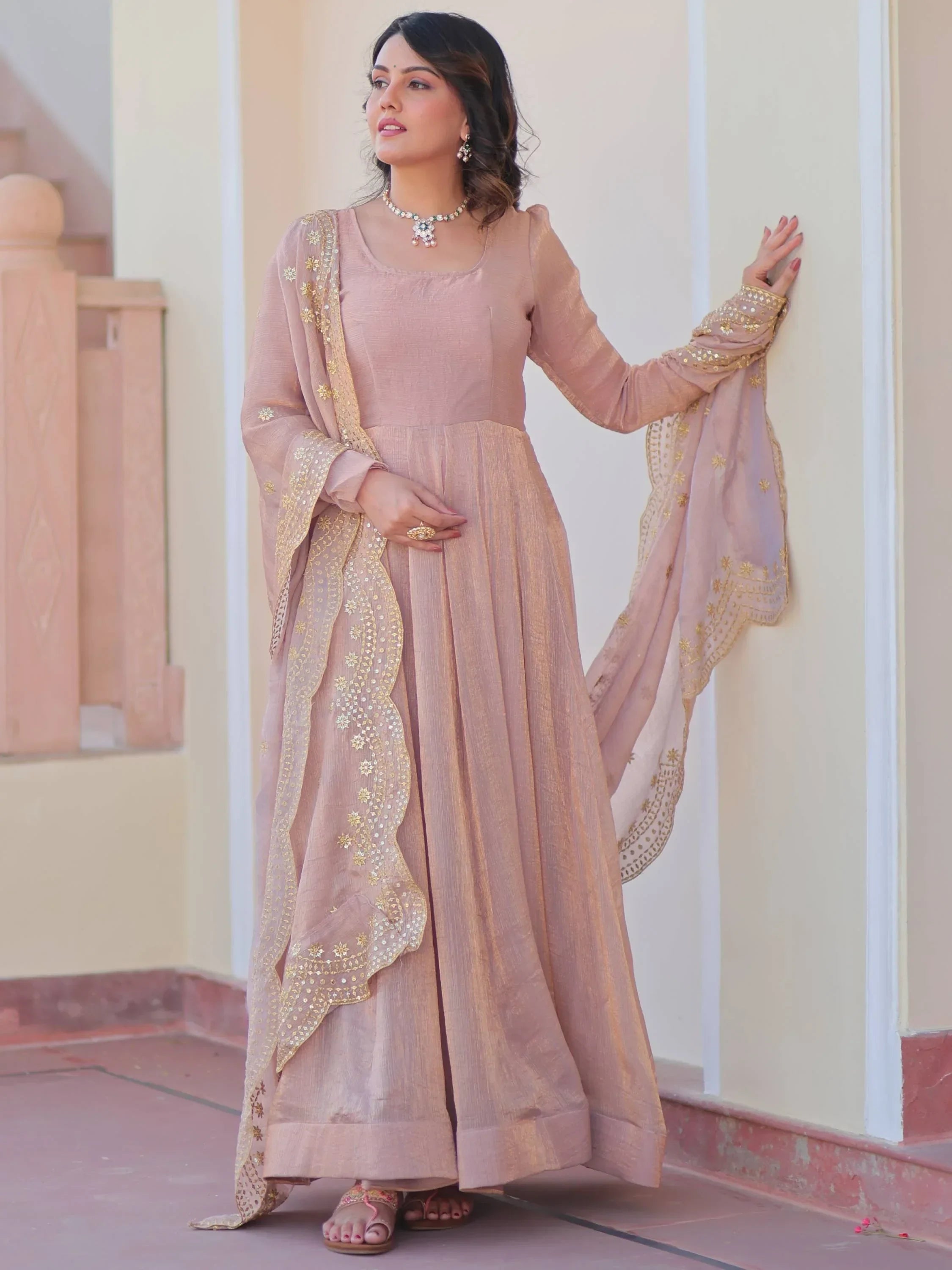 Woman in traditional chiku color ethnic gown with embroidered dupatta, standing outdoors