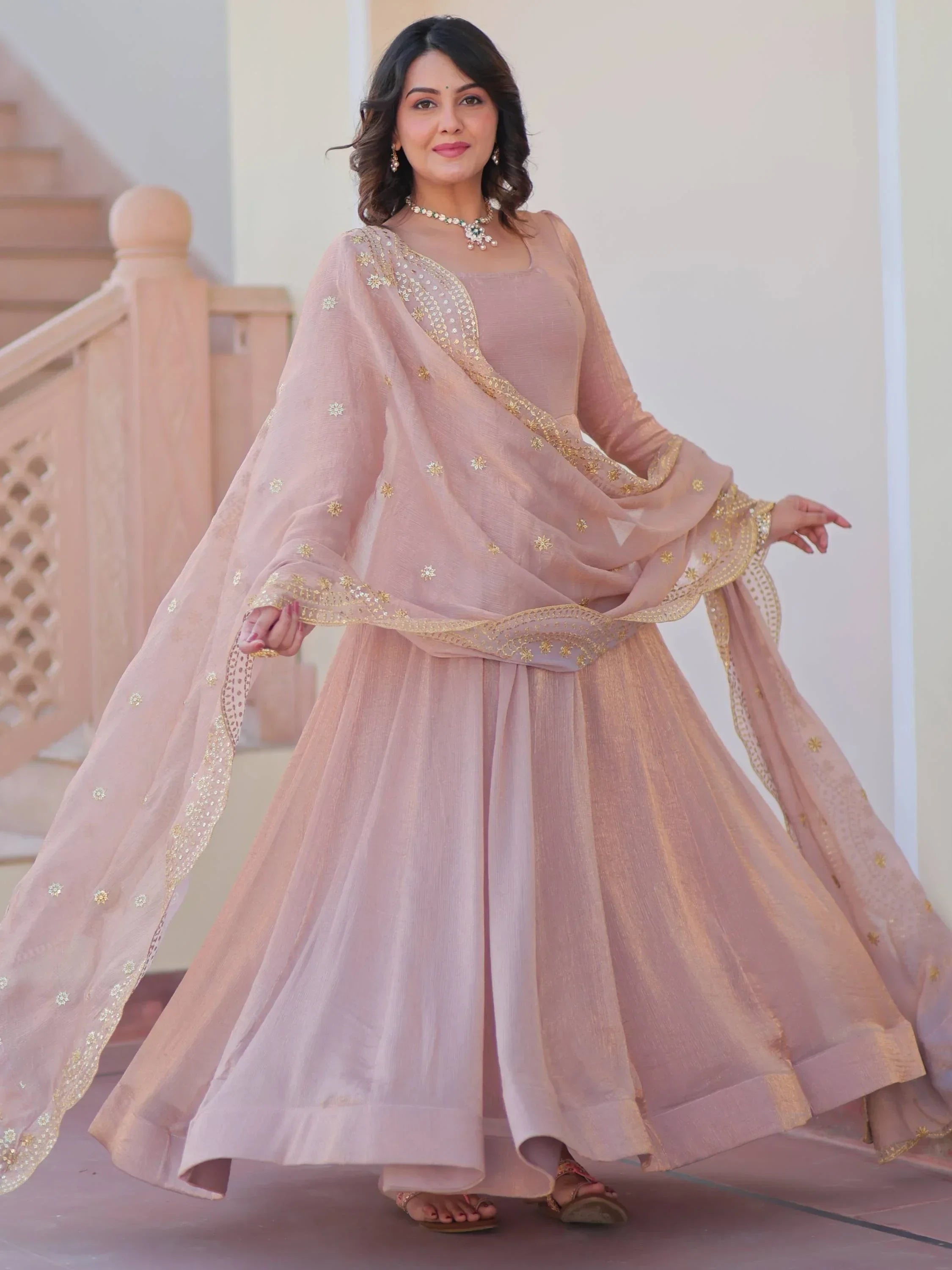 Woman in pastel pink designer lehenga choli with embroidered dupatta, ethnic jewelry