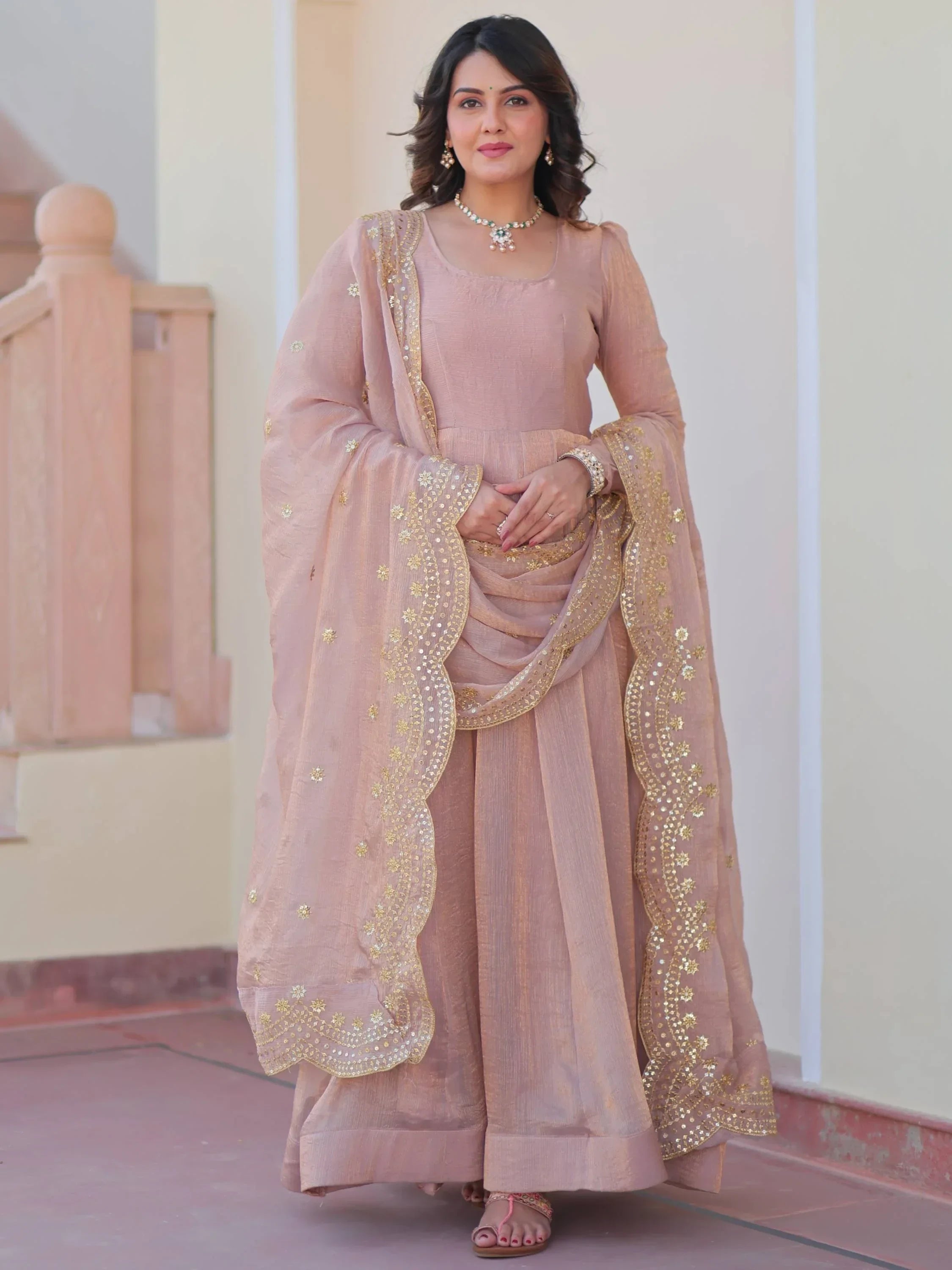 Woman wearing a beige ethnic gown with embroidered dupatta and jewelry, outdoor setting