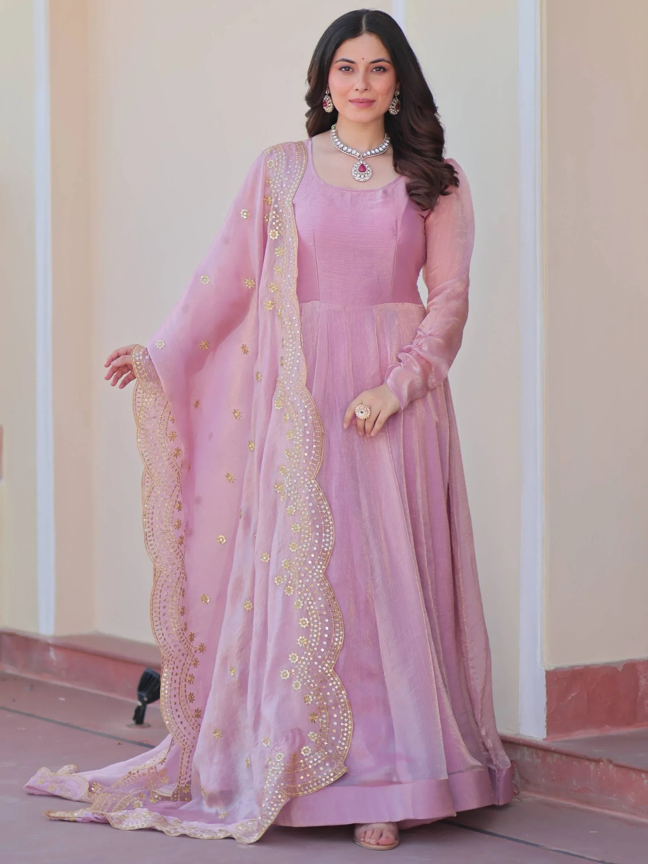 Woman wearing a pink ethnic gown with sheer dupatta and gold embroidery, traditional jewelry