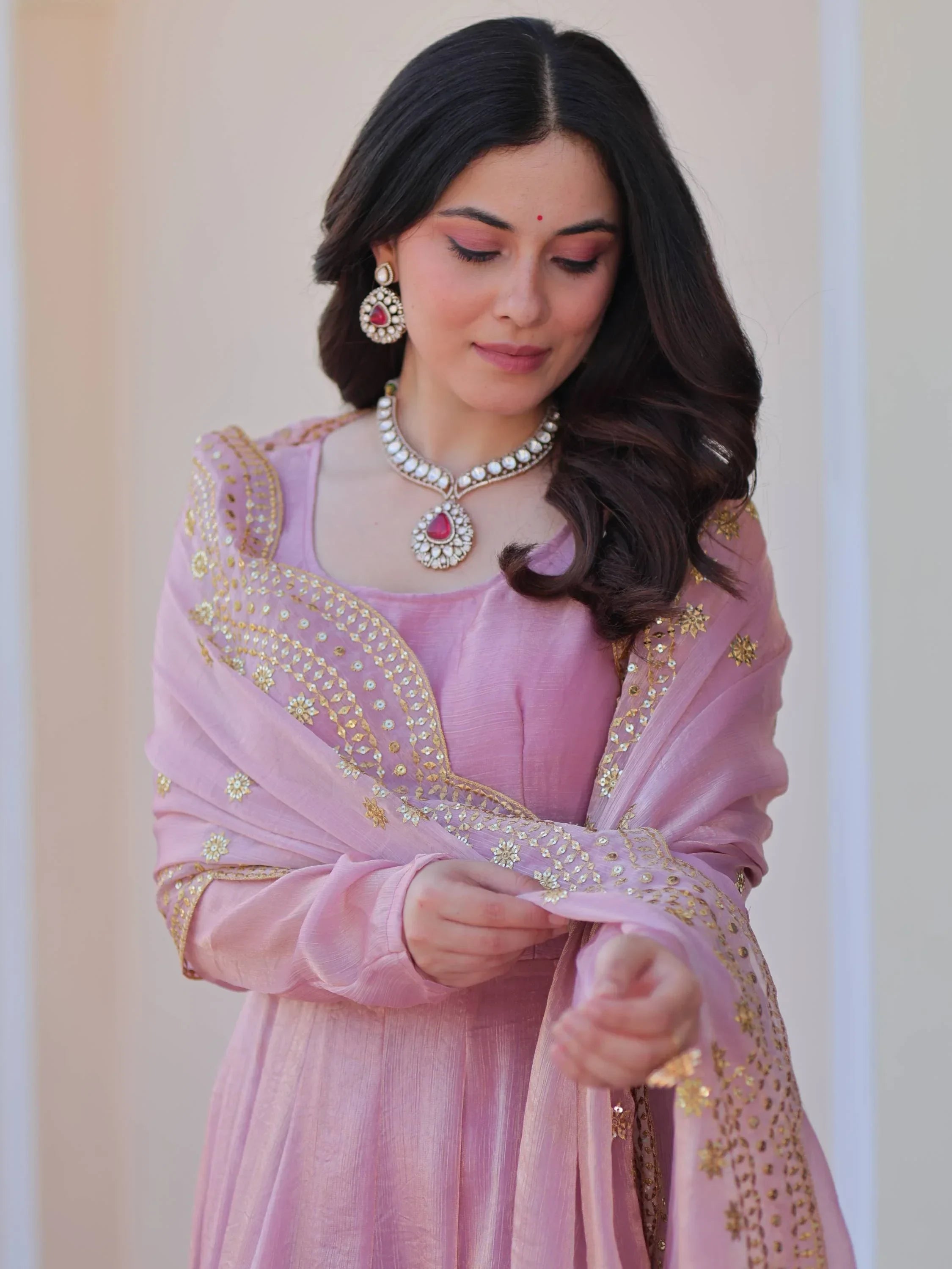 Woman in pink designer ethnic gown with gold embroidered dupatta and statement jewelry