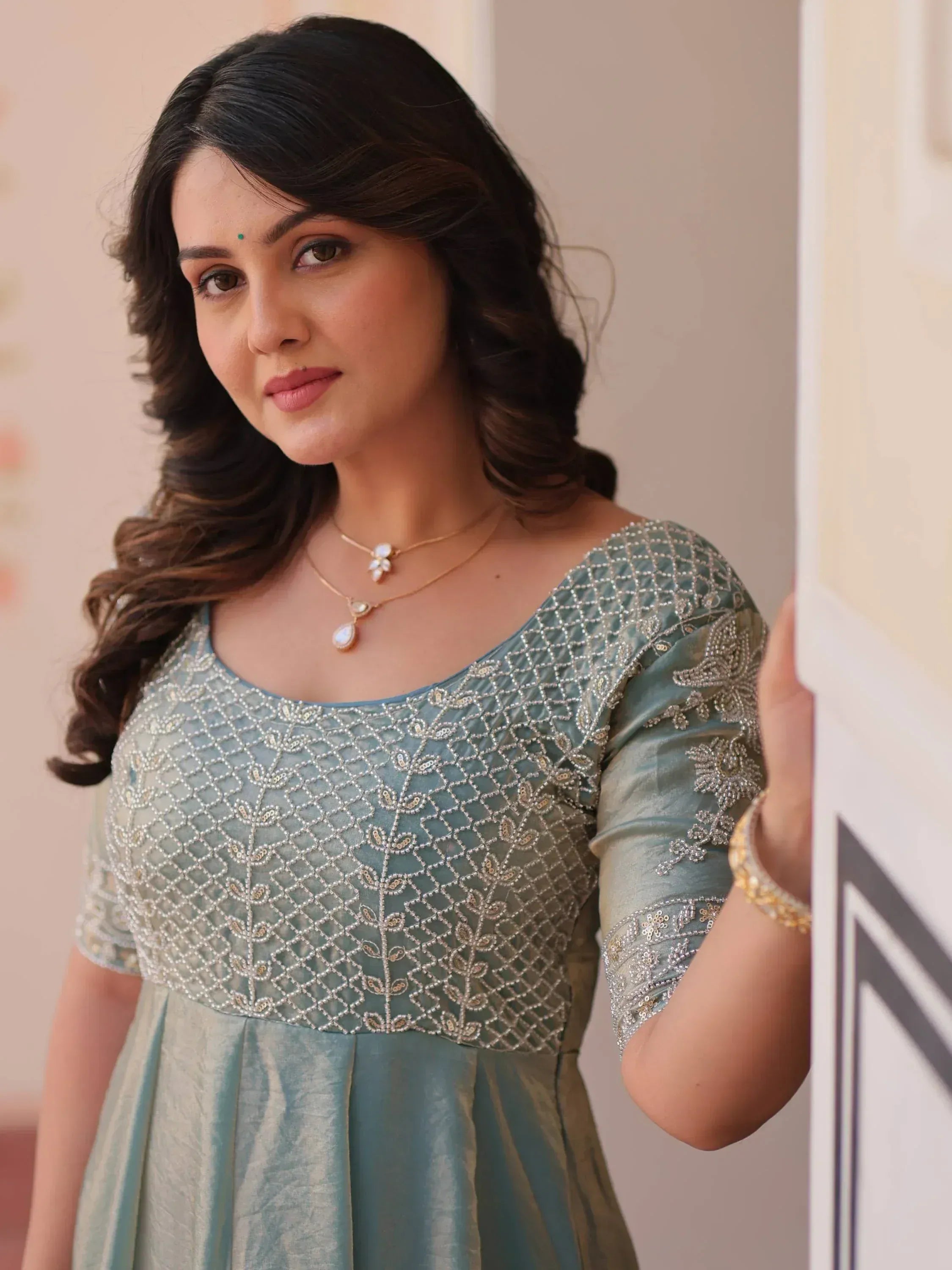 Woman in elegant light blue ethnic gown with intricate silver embroidery and pearl necklace, perfect for Indian occasions.