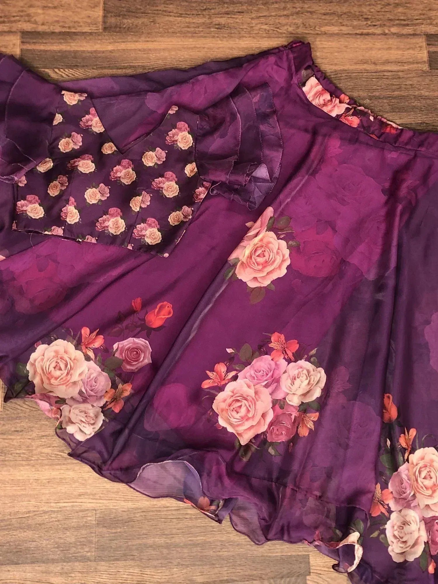 Purple floral ethnic gown with rose print, ruffled sleeves, and sheer fabric, laid on wooden floor