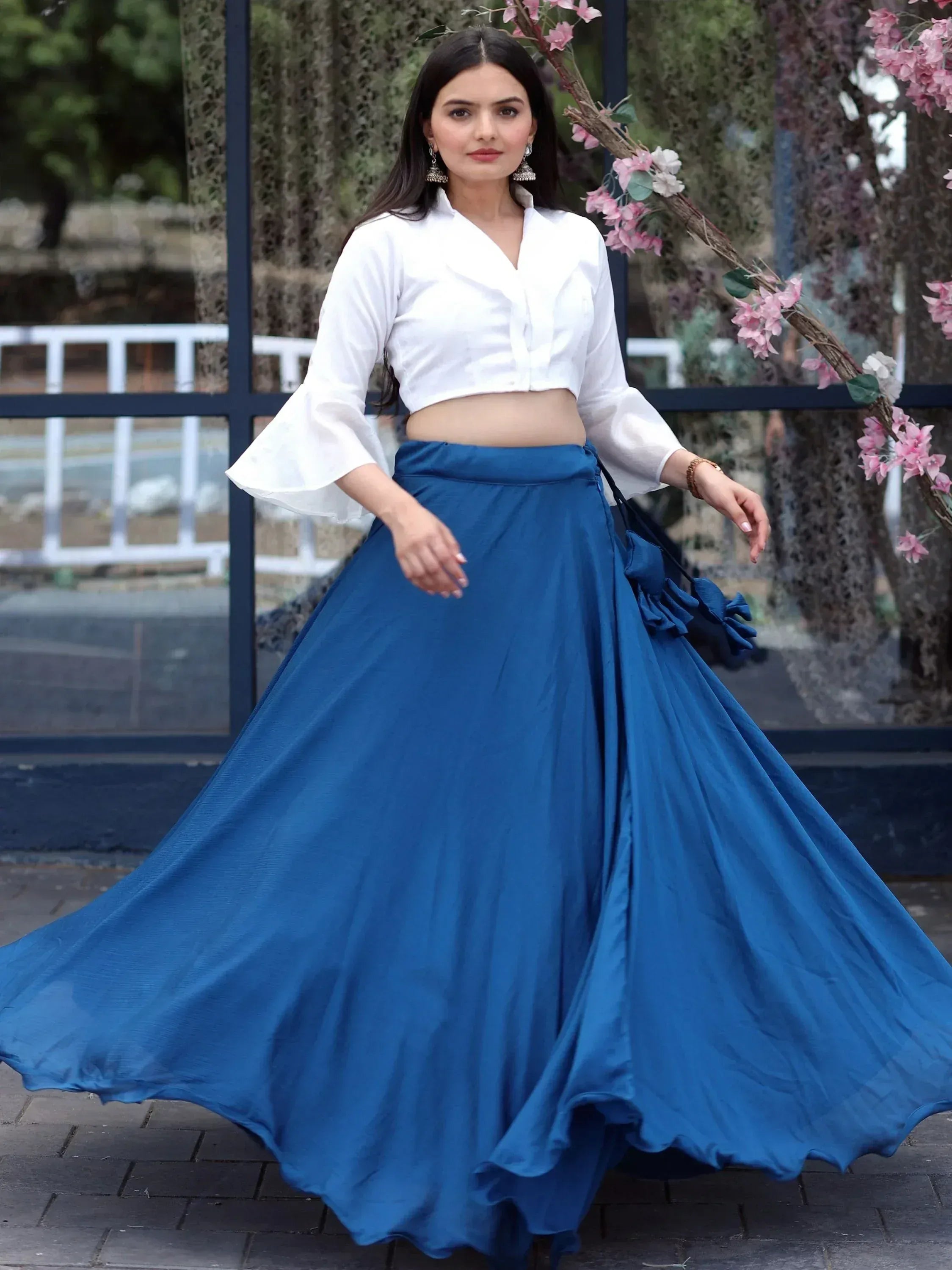 Woman in white crop top and blue flared skirt, ethnic wear outfit with floral backdrop