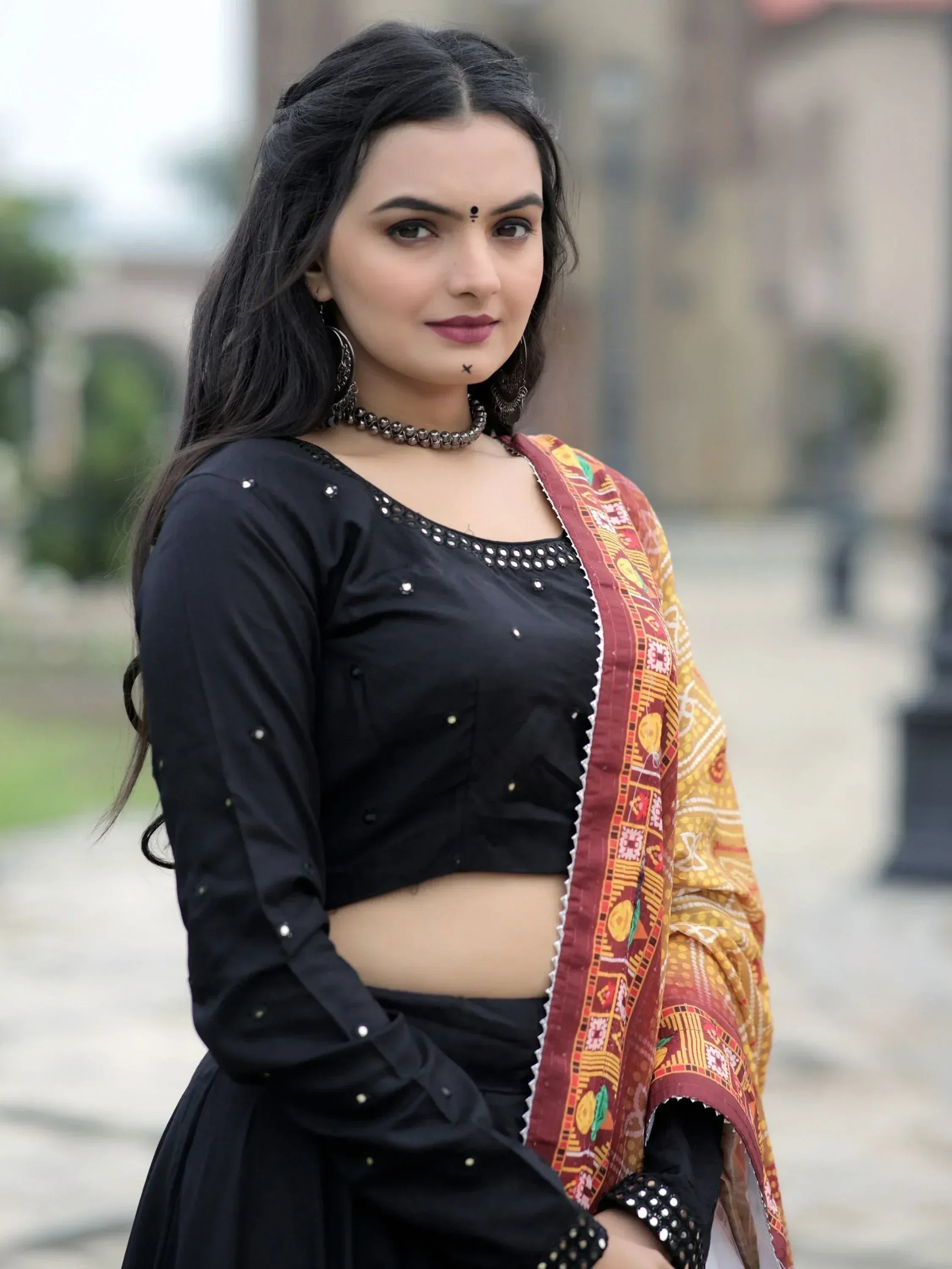 Woman in black ethnic crop top with mirror work, paired with printed dupatta, showcasing Indian fashion.