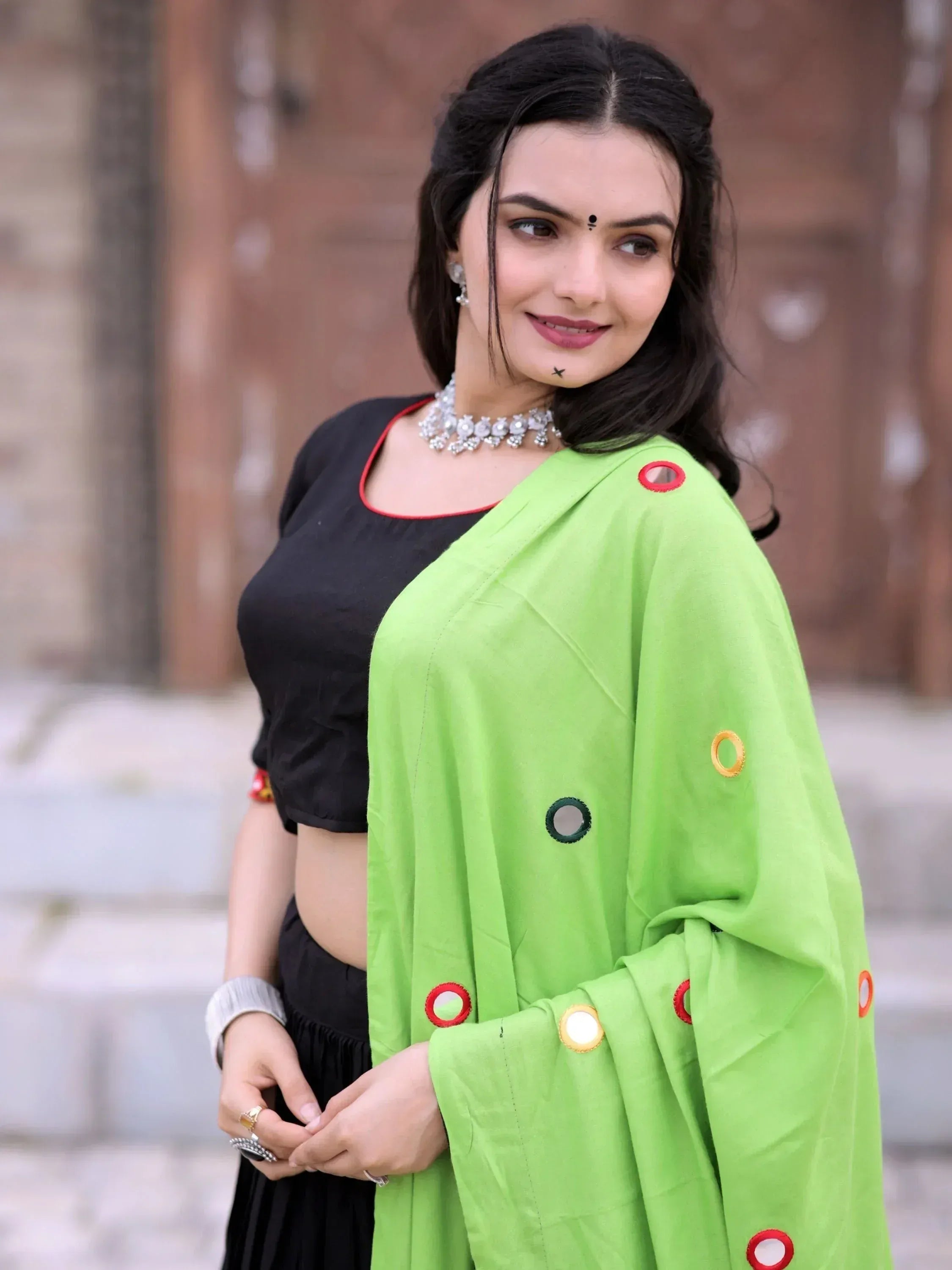 Woman in vibrant green saree with mirror work, paired with black blouse and ethnic jewelry