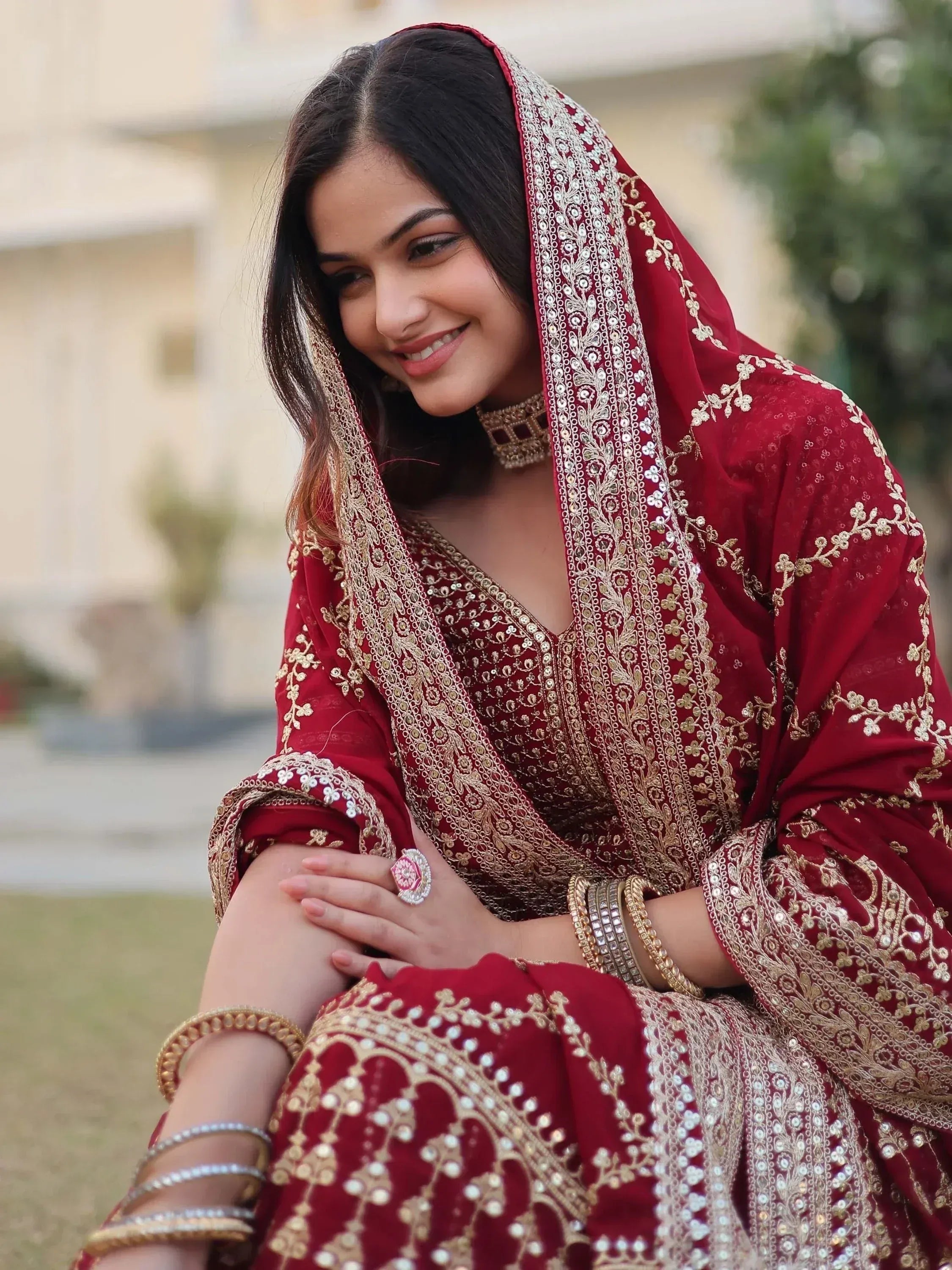 Woman in maroon embroidered Indian ethnic wear with gold detailing, perfect for weddings or festive occasions.