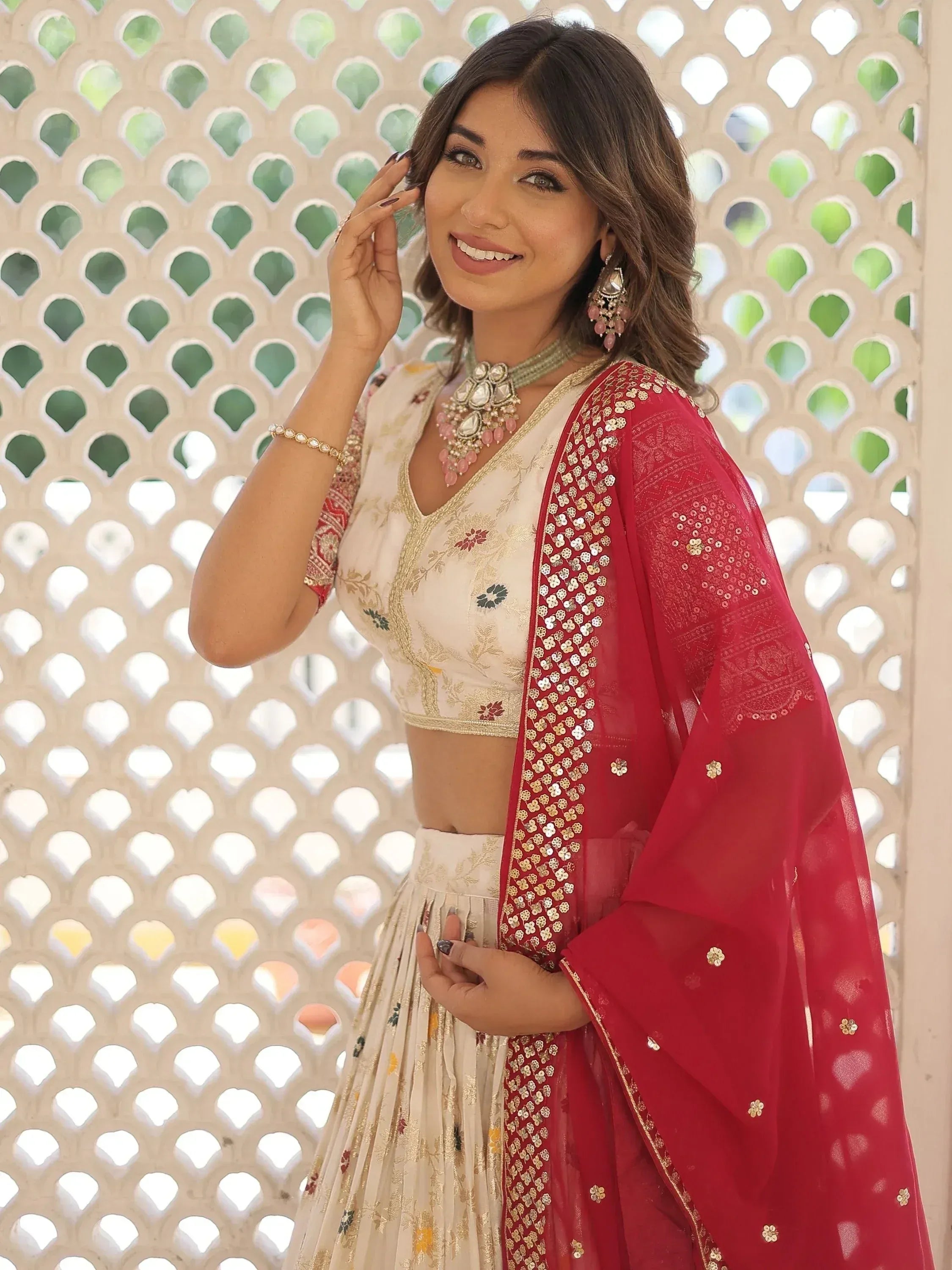 Woman in elegant designer lehenga choli with red dupatta, floral embroidery, and traditional jewelry.