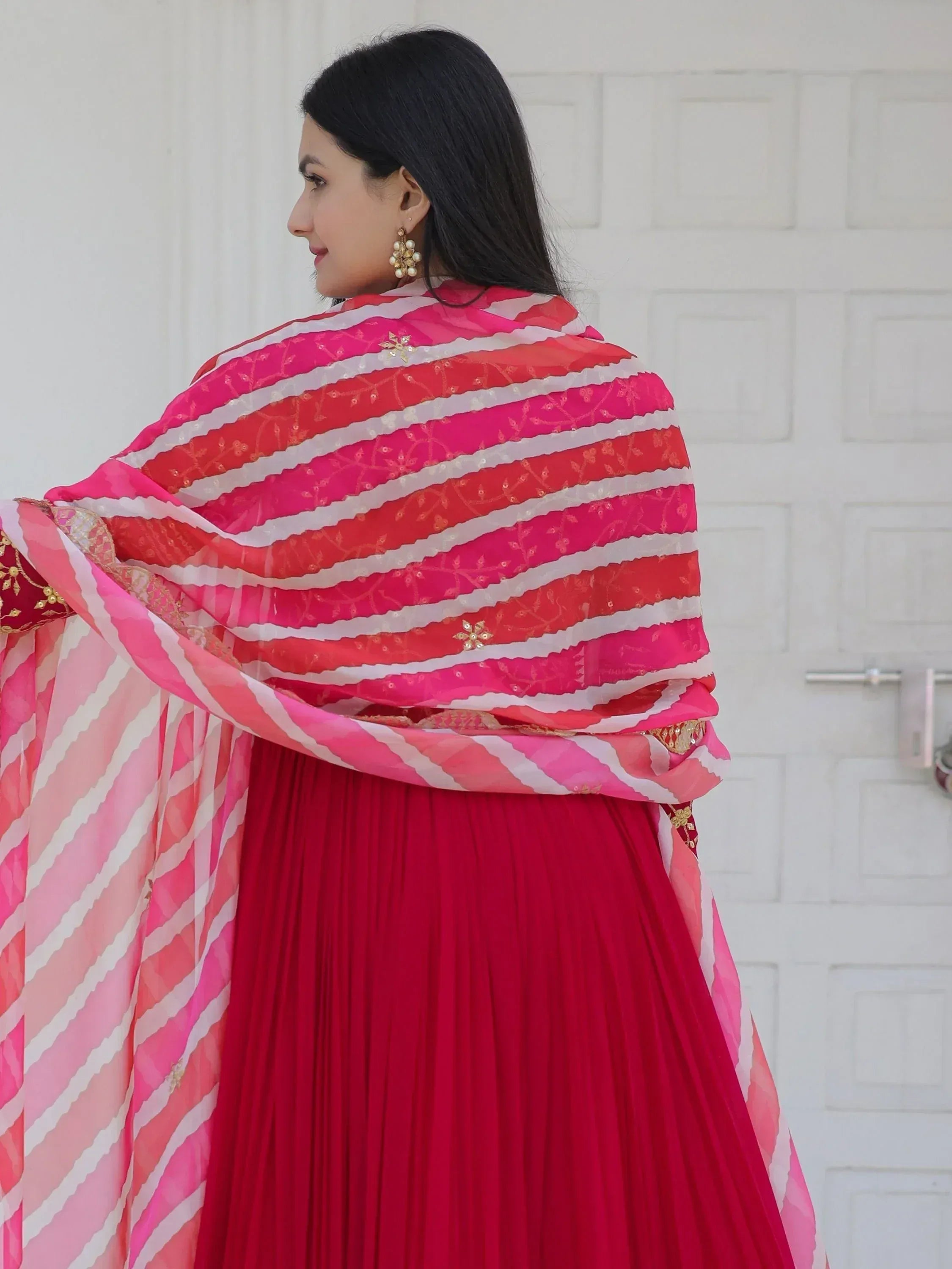 Woman in red ethnic gown with pink and white striped dupatta, gold embroidery, and pearl earrings
