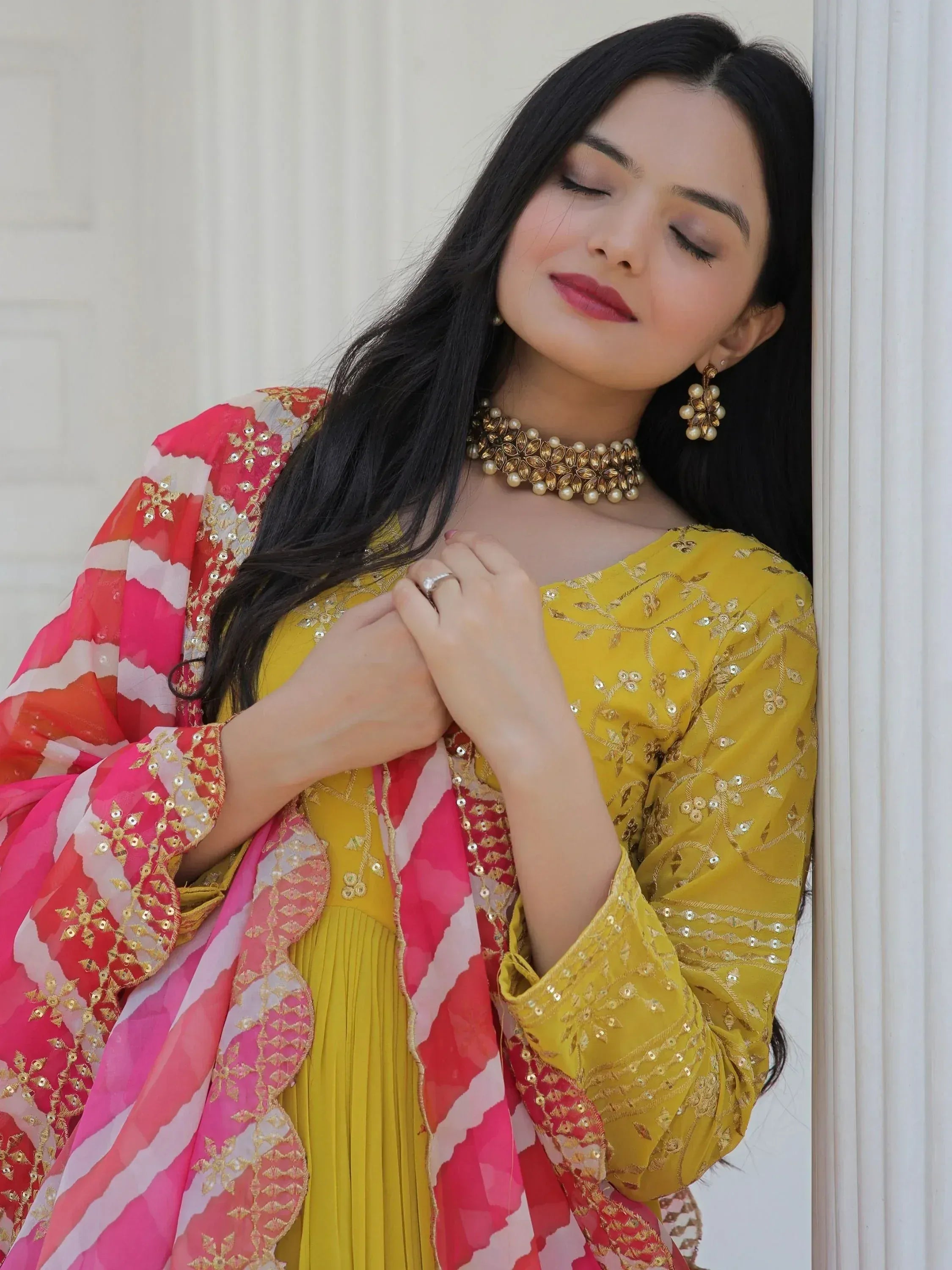 Woman in yellow embroidered salwar kameez with pink dupatta, gold jewelry, ethnic wear