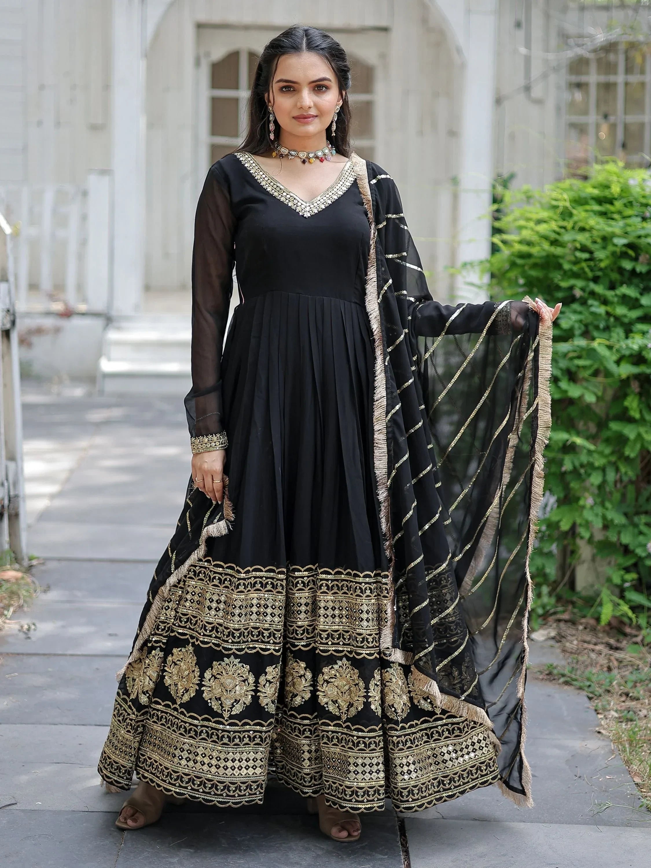 Woman wearing black Anarkali suit with gold embroidery and matching dupatta, outdoor setting