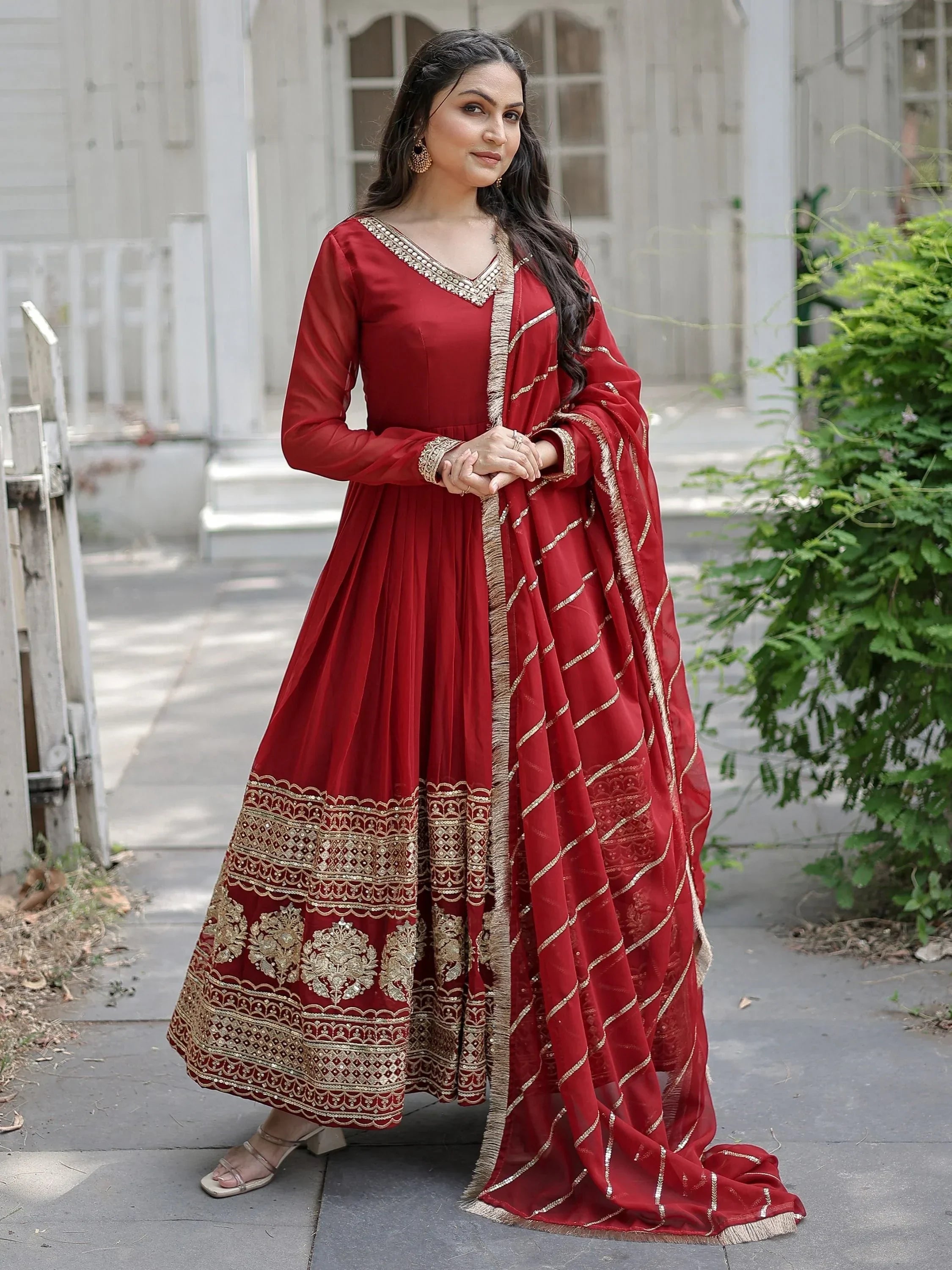 Woman in maroon Anarkali suit with gold embroidery and dupatta, posing outdoors