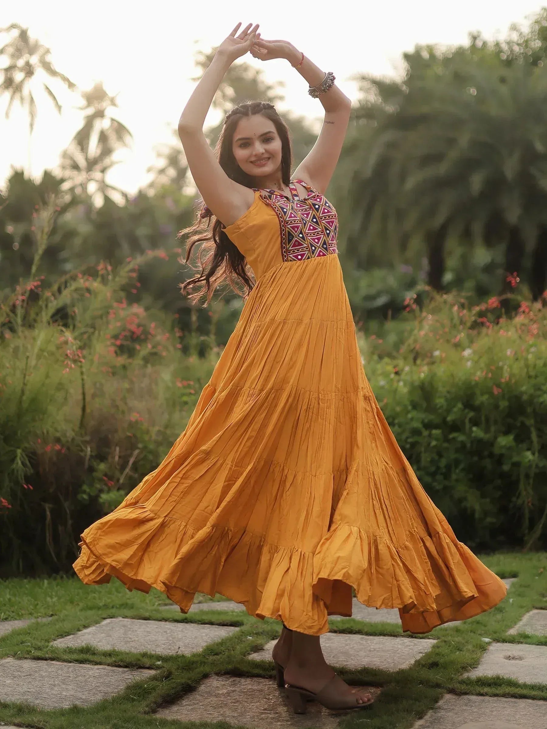 Woman in mustard yellow ethnic gown with embroidered bodice, twirling in garden