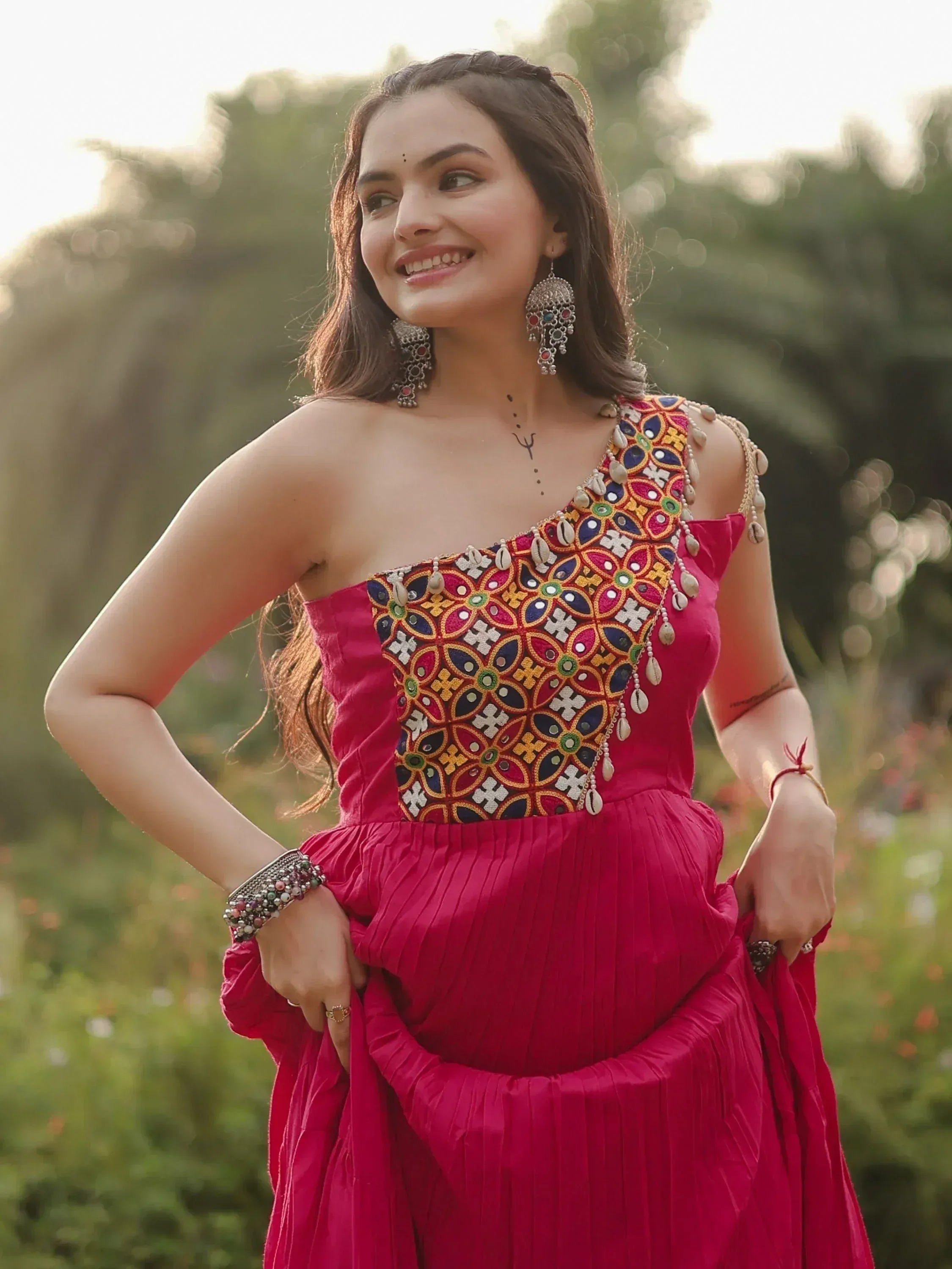 Woman in vibrant pink ethnic gown with colorful mirror and shell embroidery, perfect for Indian festive occasions.