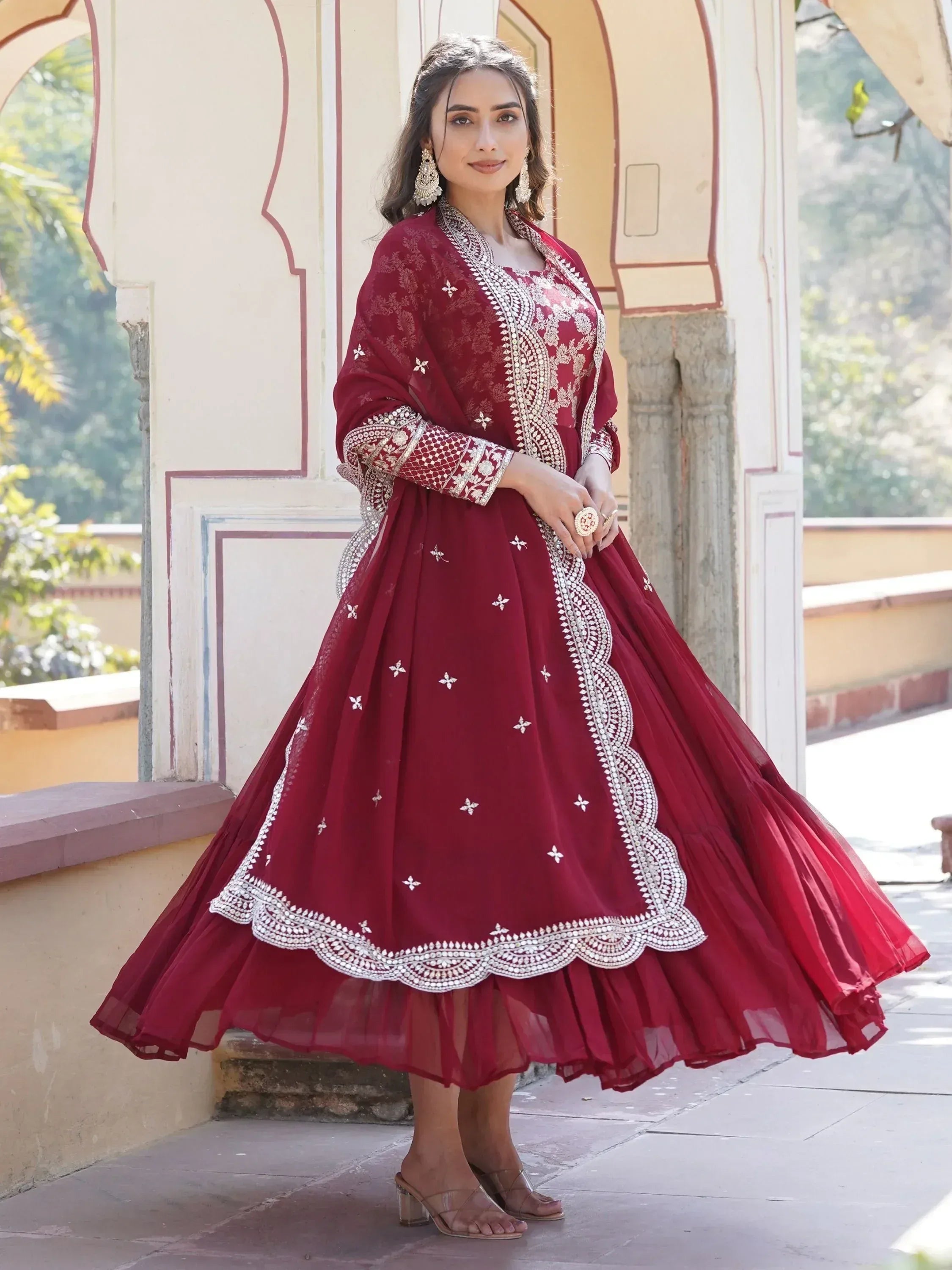 Woman in maroon embroidered Anarkali suit with dupatta, ethnic Indian attire outdoors