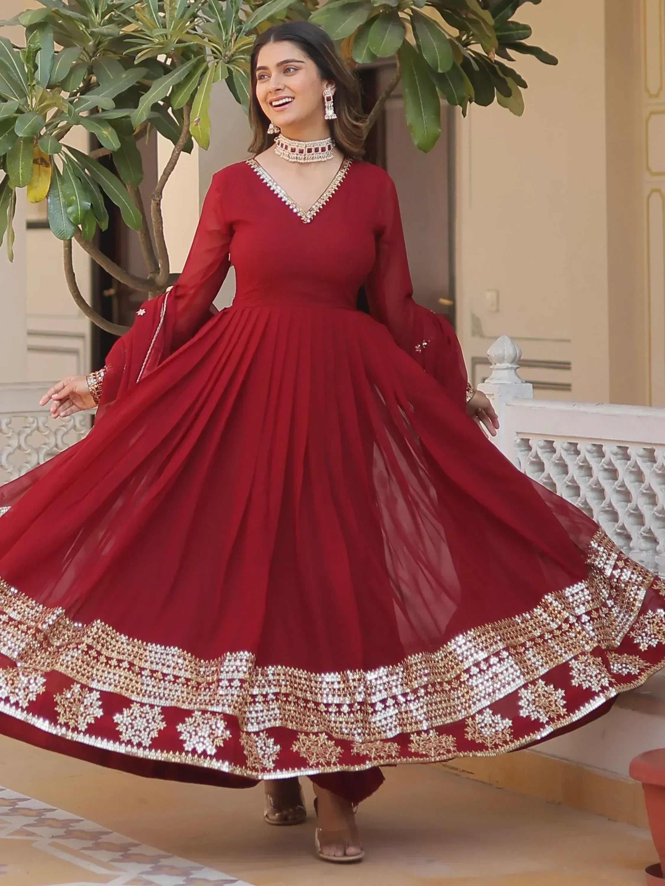 Woman in maroon ethnic gown with gold embroidery, perfect for Indian weddings or festive occasions.