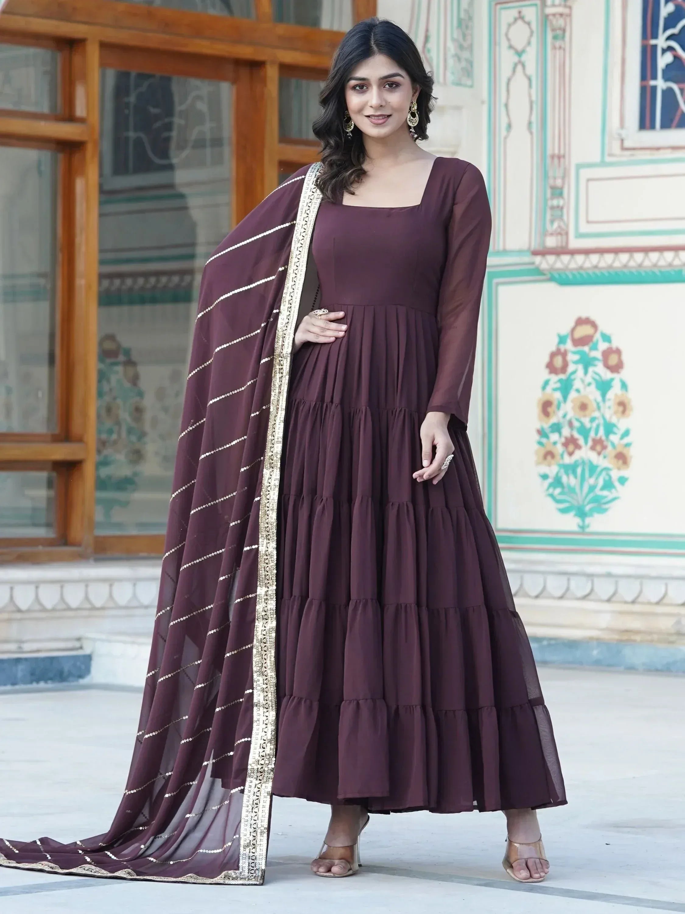 Woman wearing a brown ethnic gown with gold border dupatta, traditional earrings, outdoor setting