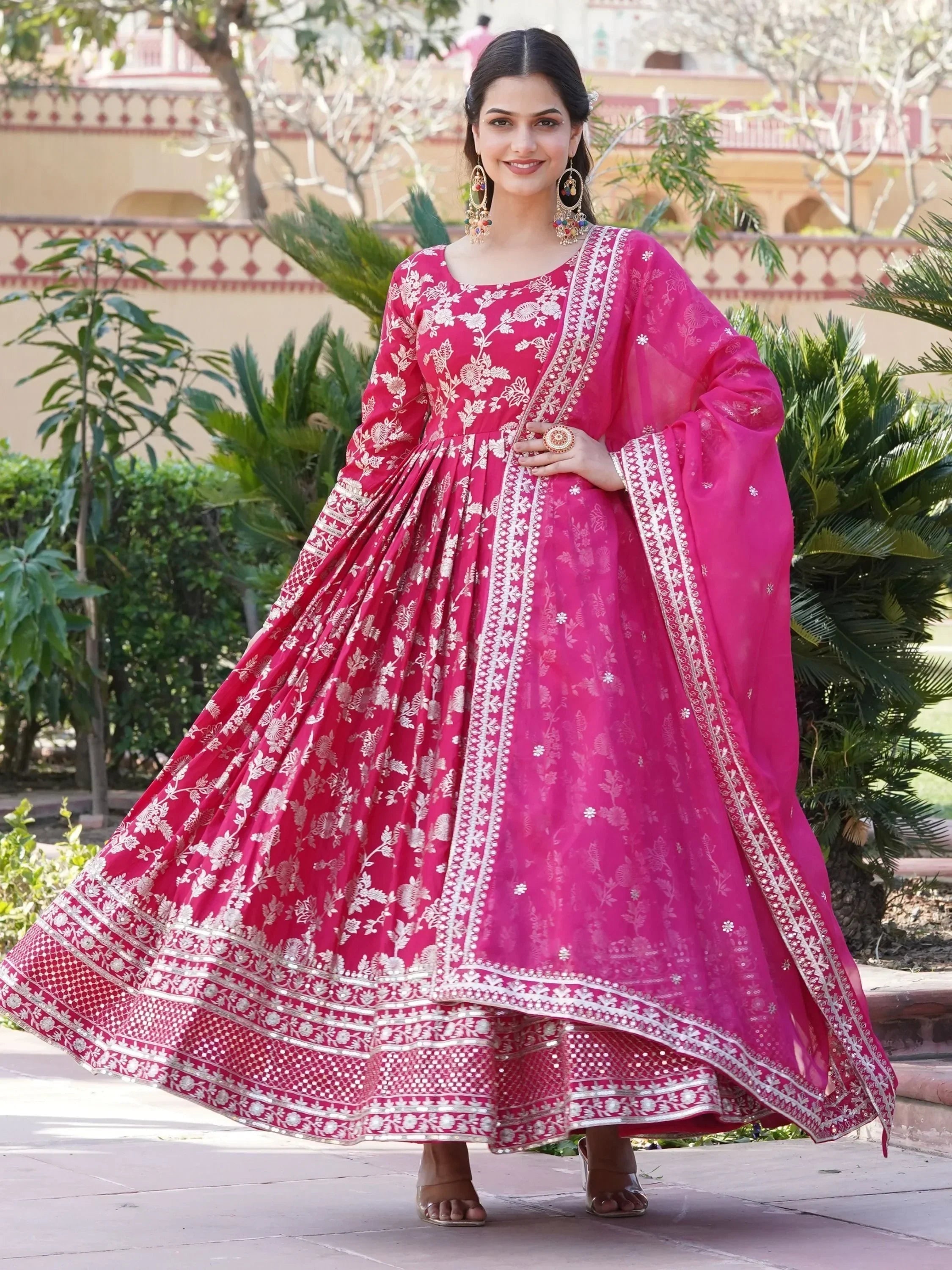 Woman wearing pink floral embroidered lehenga choli with dupatta, standing outdoors