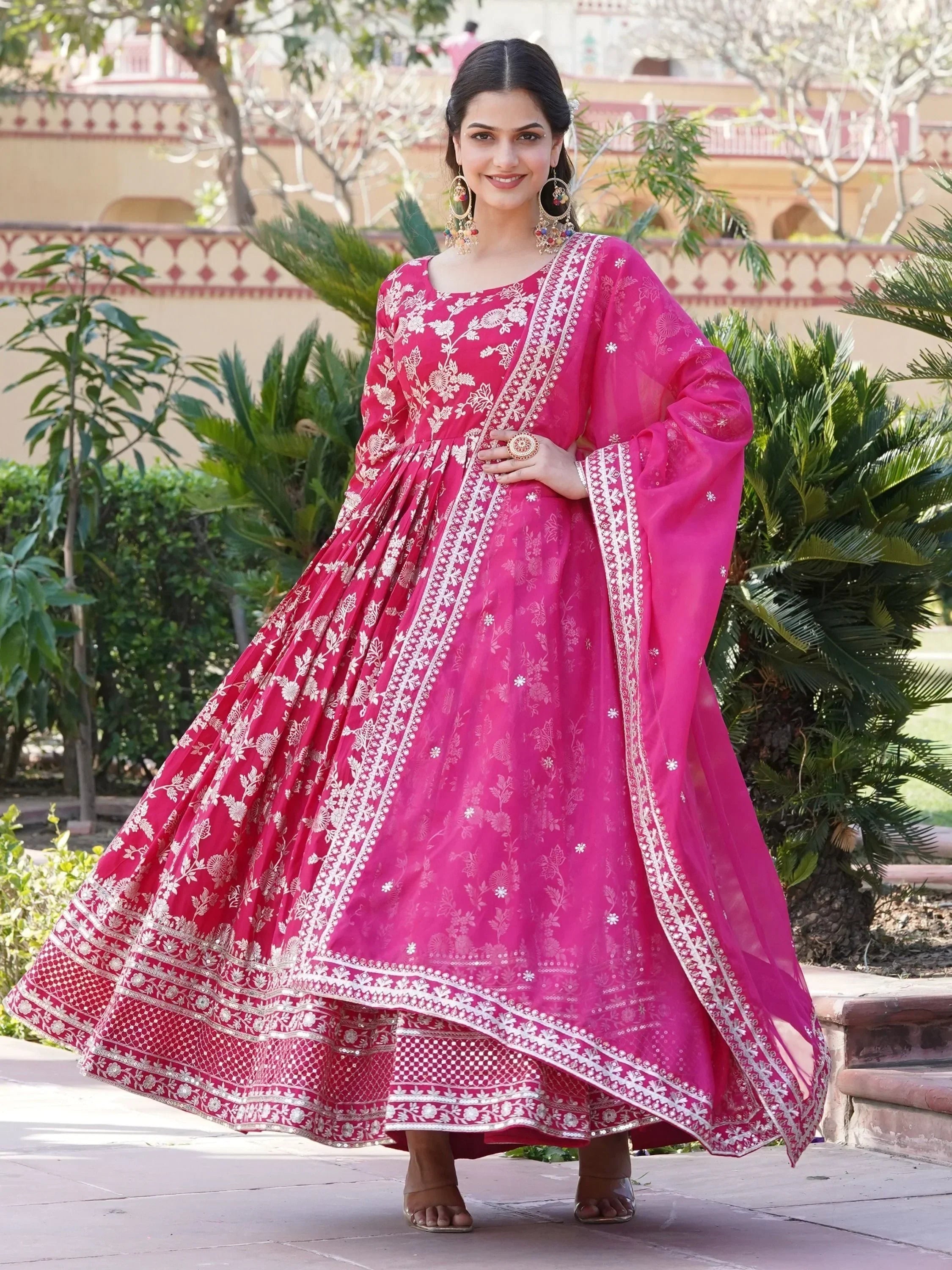Woman wearing a pink floral embroidered Anarkali suit with matching dupatta outdoors