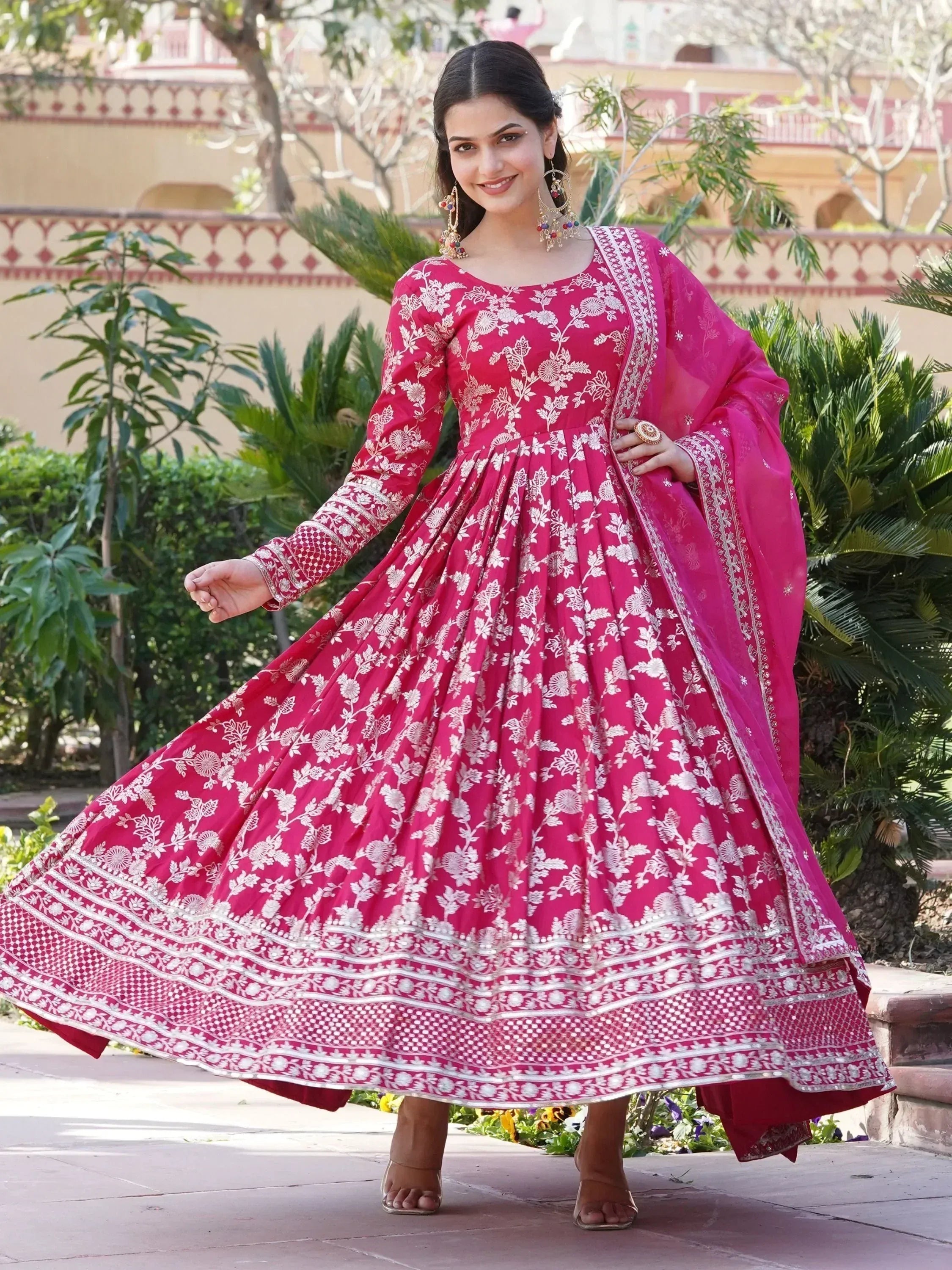 Woman in pink floral embroidered Anarkali gown with dupatta, outdoor garden setting
