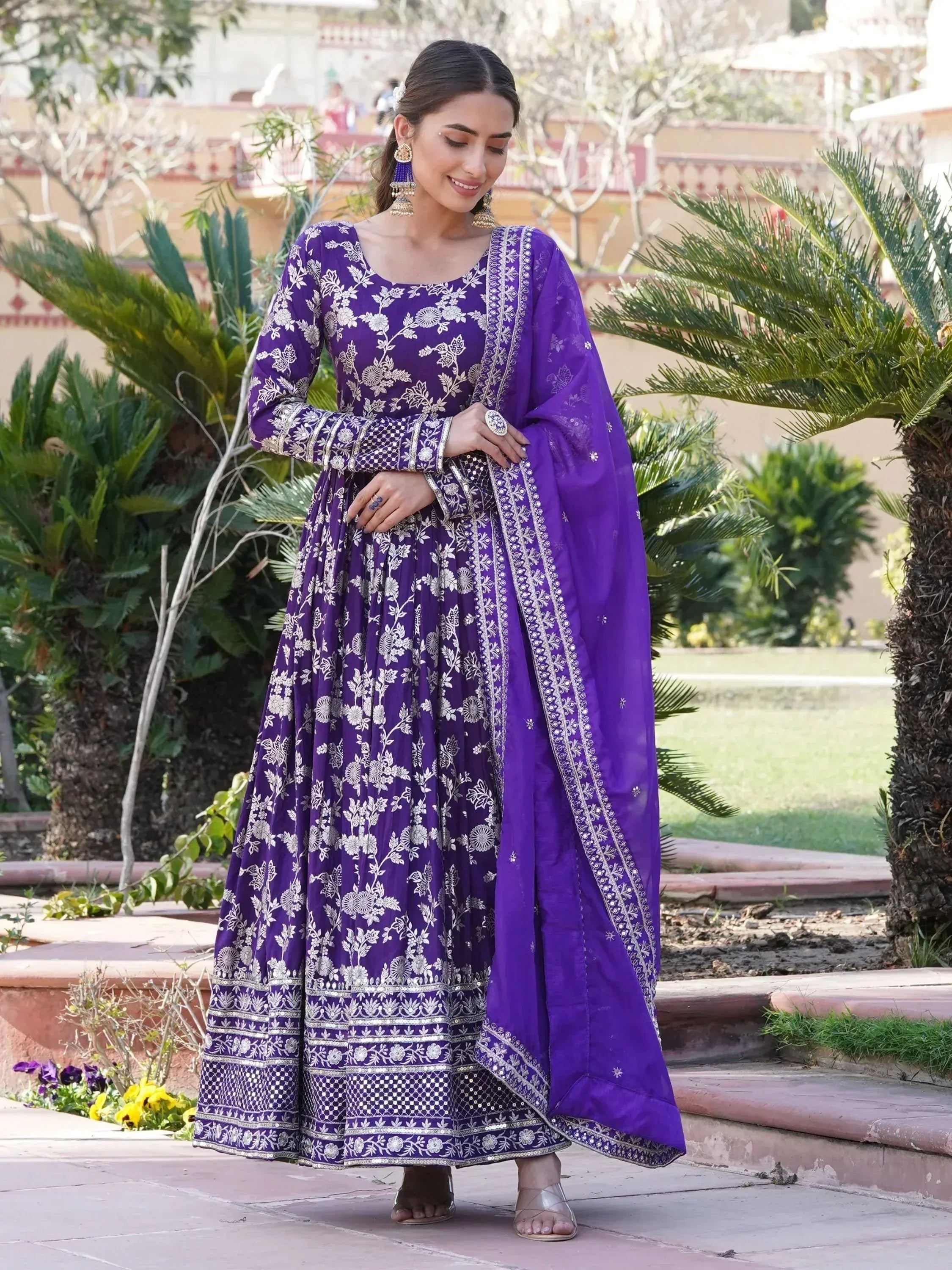 Woman in a purple embroidered ethnic gown with matching dupatta, standing outdoors
