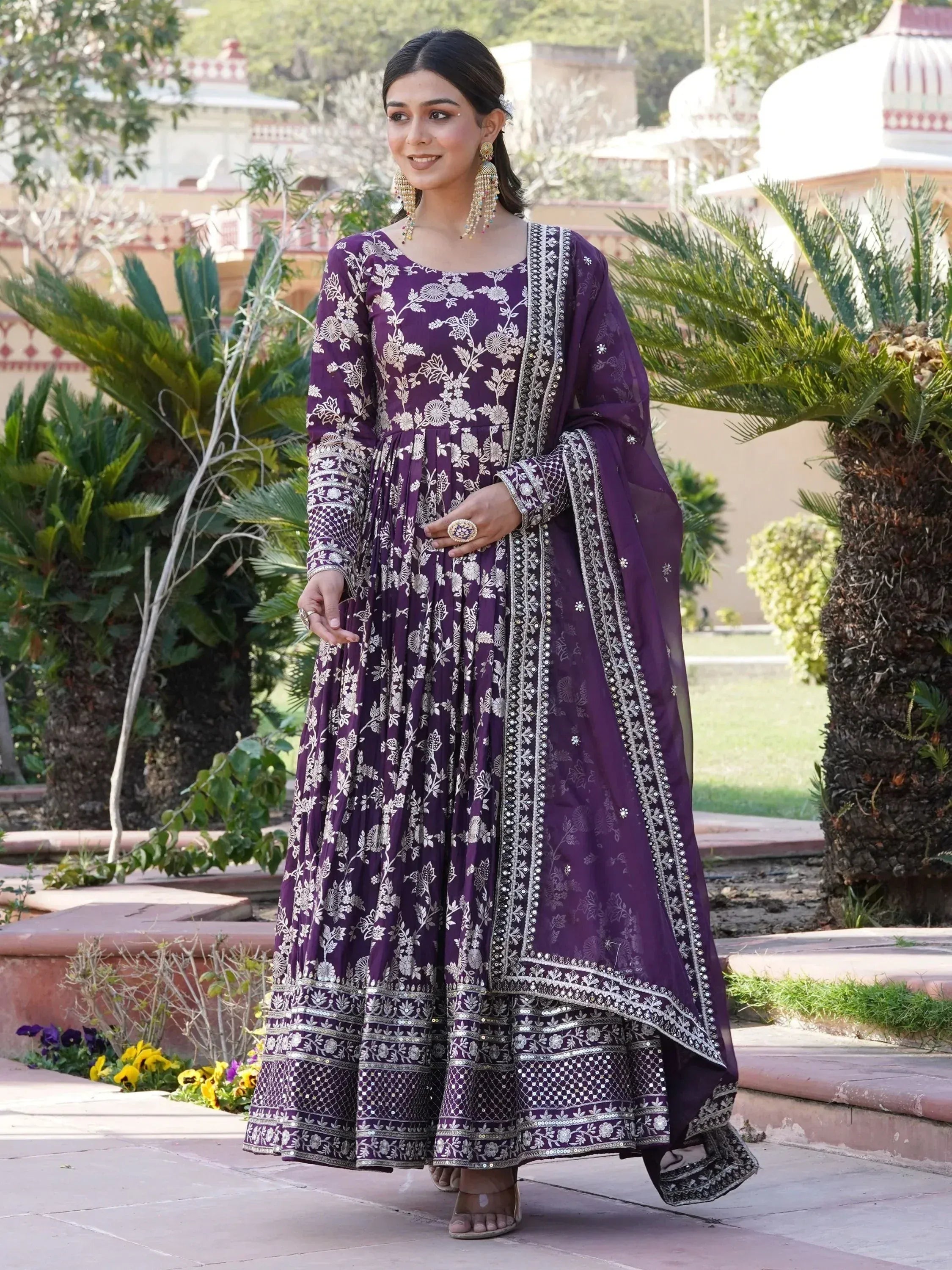 Woman in a purple embroidered Anarkali gown with dupatta, outdoor garden setting