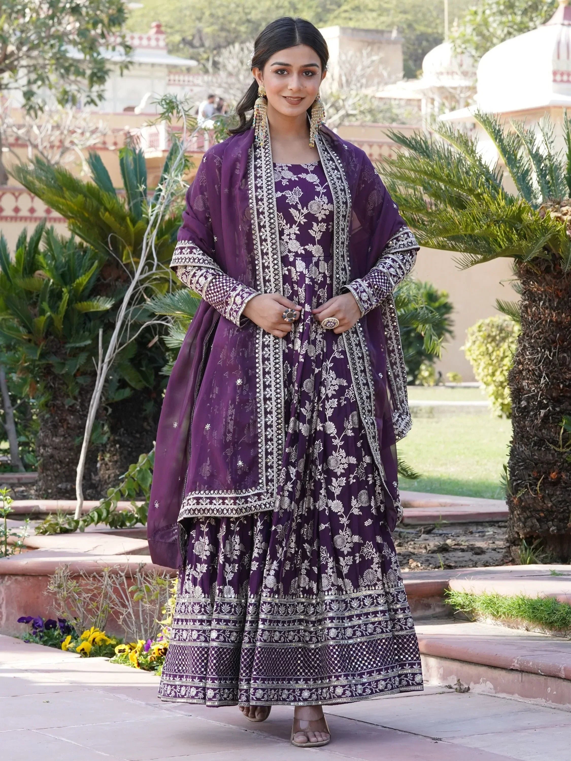 Woman wearing a purple embroidered ethnic gown with dupatta, outdoor garden setting