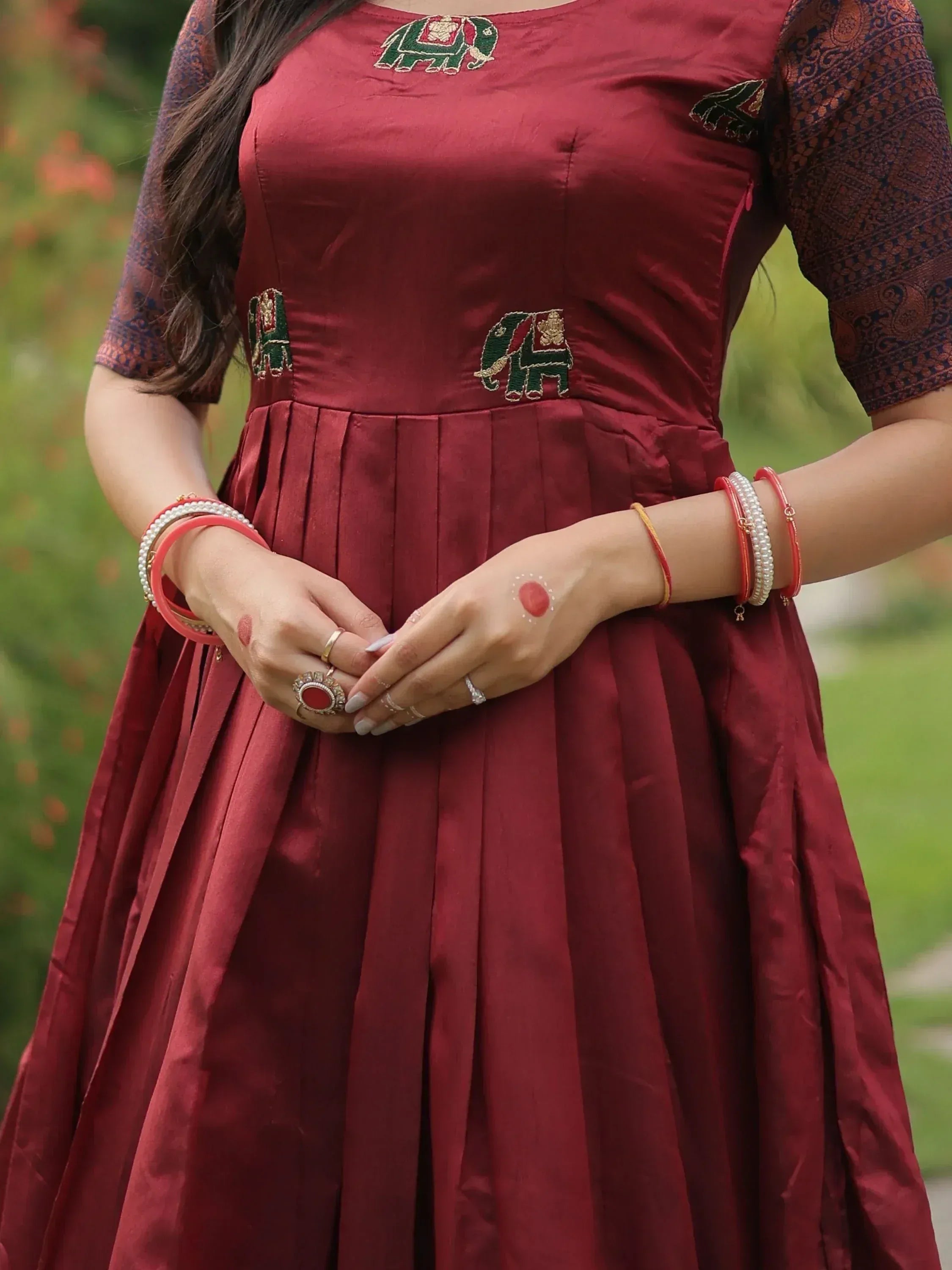 Maroon ethnic gown with elephant embroidery, pleated skirt, and traditional jewelry for Indian wear