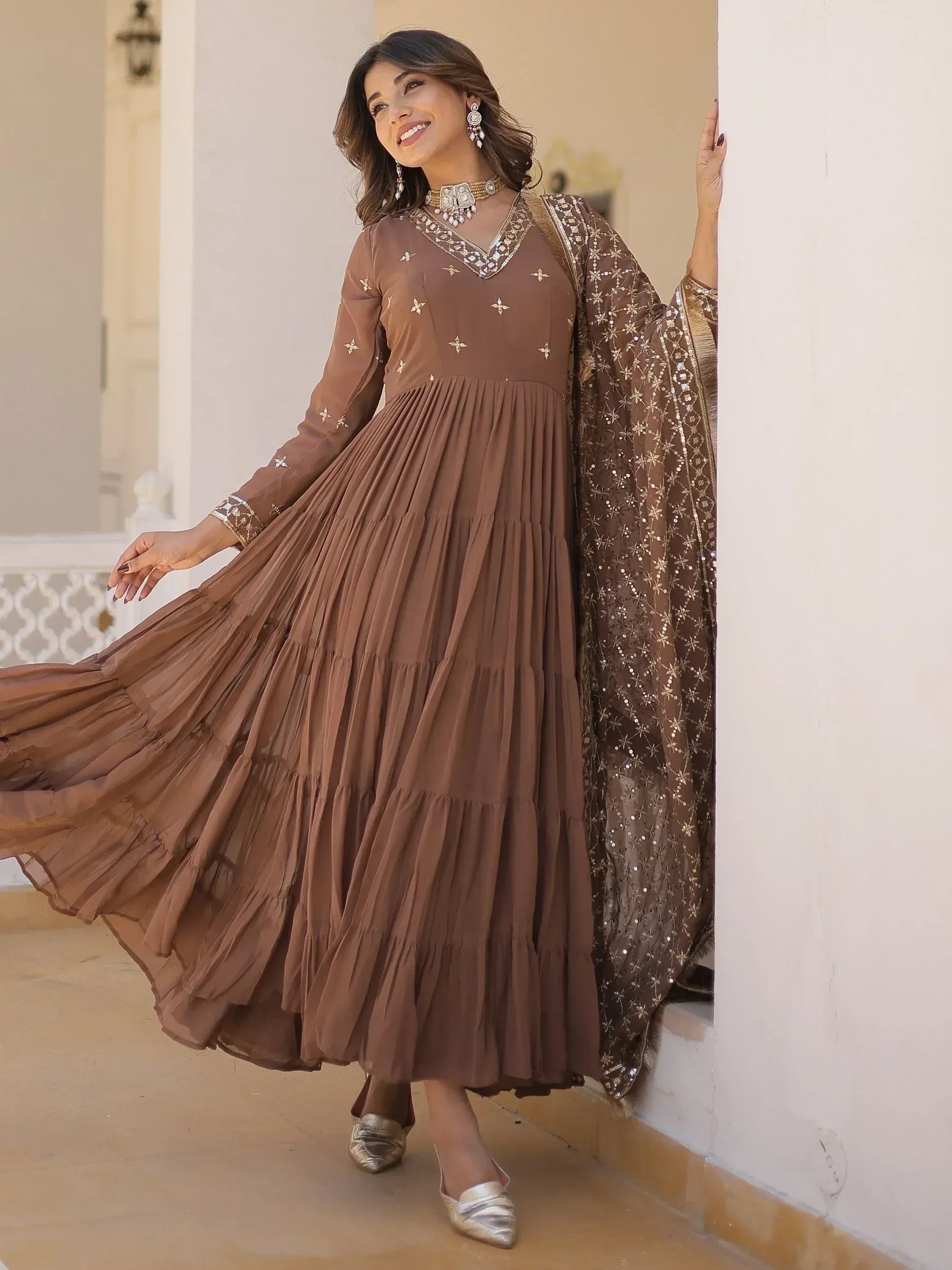Brown ethnic gown with gold embroidery and pleated skirt, paired with matching dupatta and statement jewelry