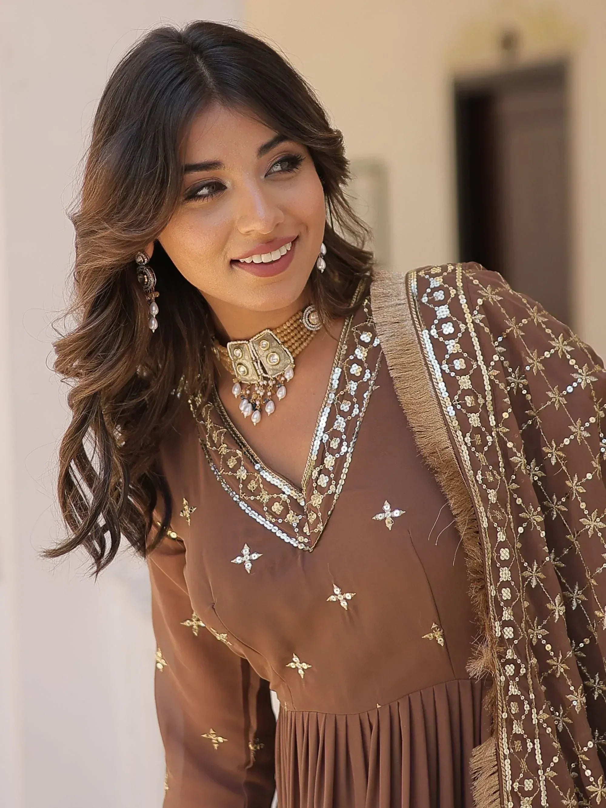 Woman in brown embroidered ethnic gown with gold sequin detailing and matching jewelry